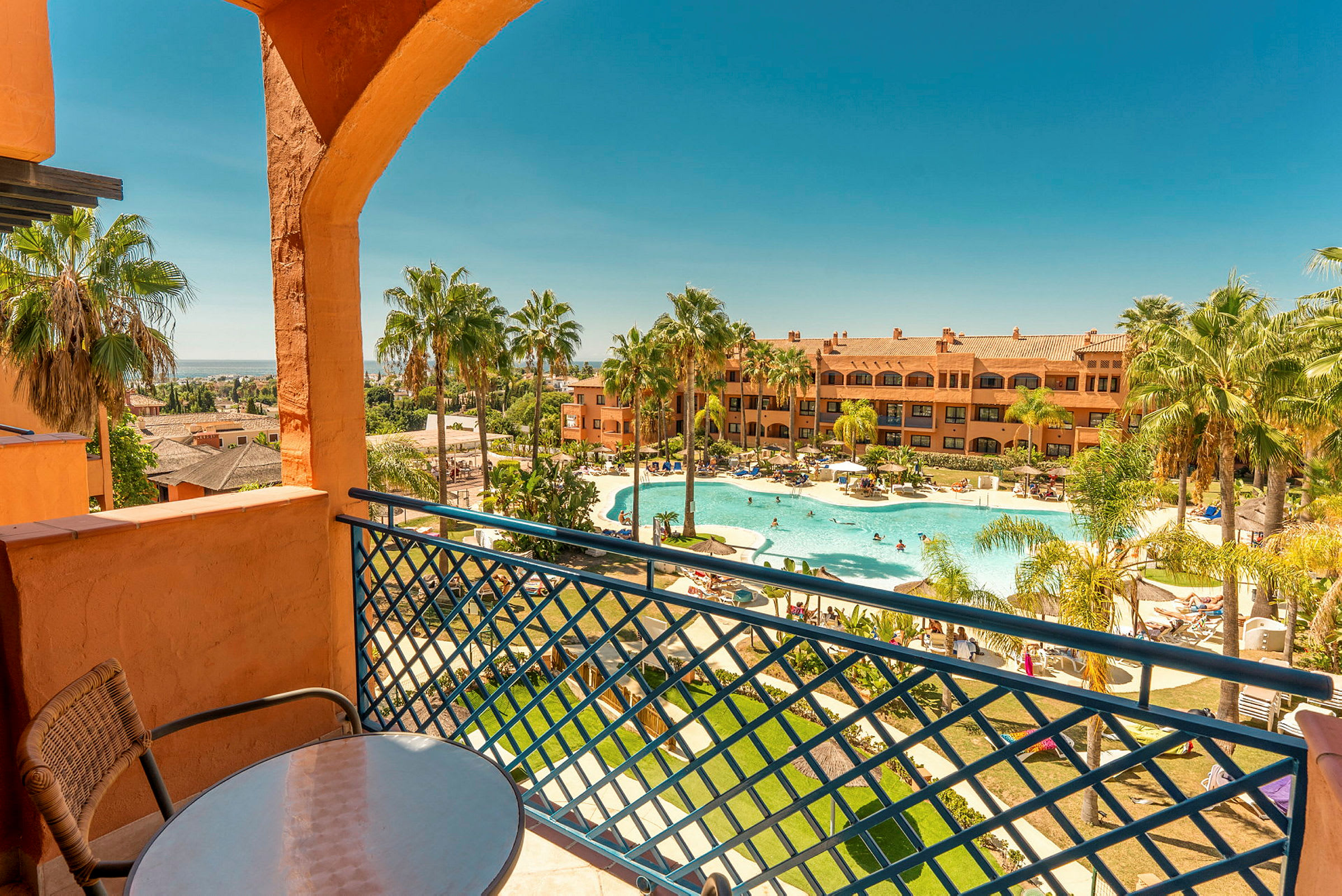 En balkong med utsikt över en swimmingpool och byggnader i tropisk miljö. (AI-genererad text)