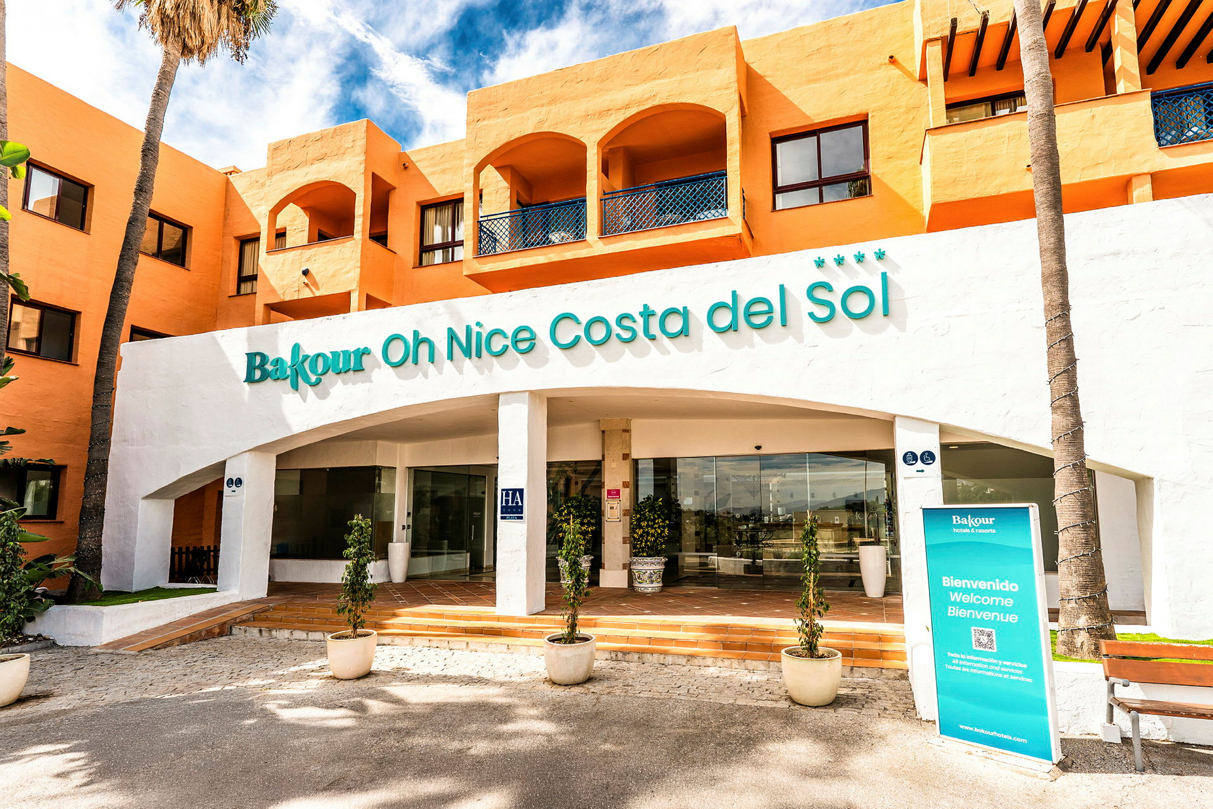 Fasad av ett hotell med orange väggar och skylt där det står "Bakour Oh Nice Costa del Sol". (AI-genererad text)