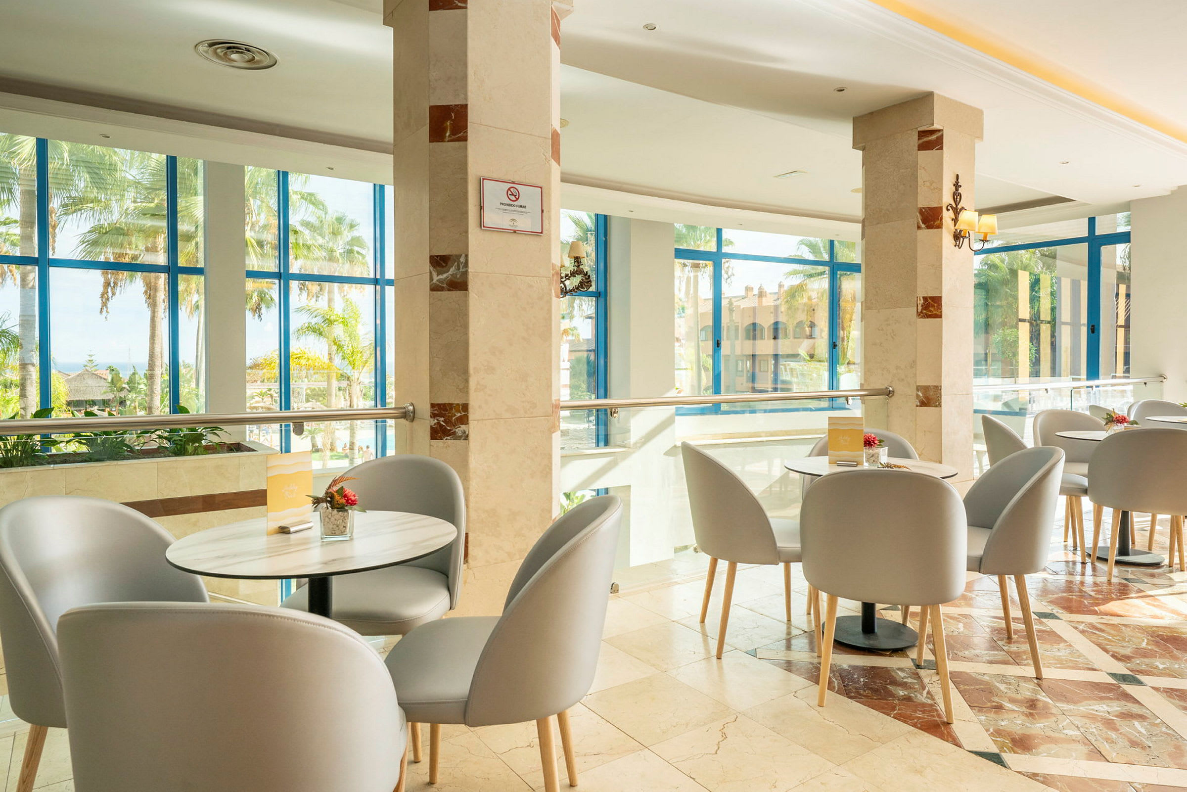 Ljus restaurangmiljö med bord och stolar samt stora fönster som vetter mot trädgården. (AI-genererad text)