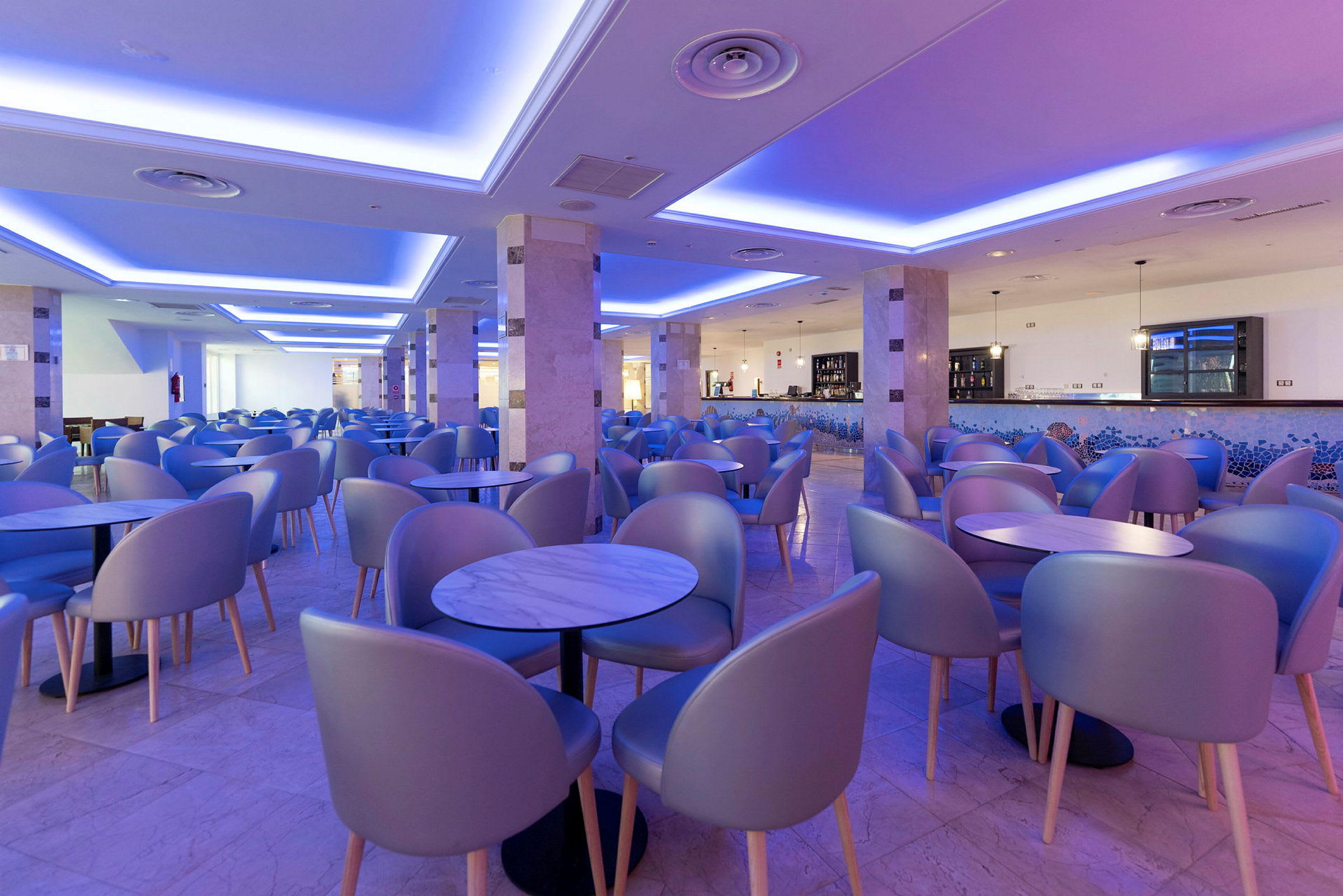 Interiör av en restaurang eller lounge med moderna stolar och bord, belyst med blått och lila ljus. (AI-genererad text)