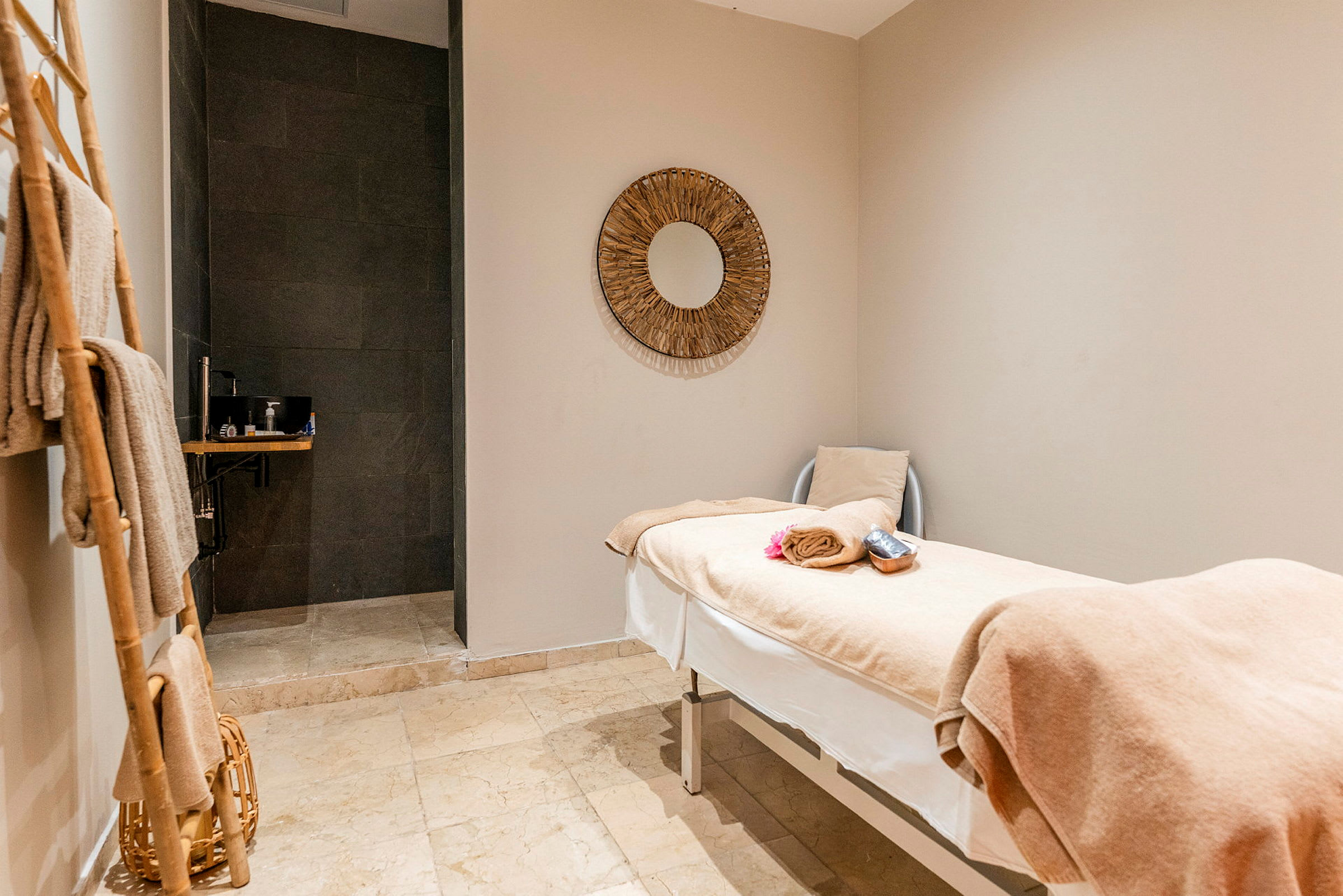 Ett behandlingsrum med en massagebänk täckt av beige handdukar och en spegel på väggen. (AI-genererad text)