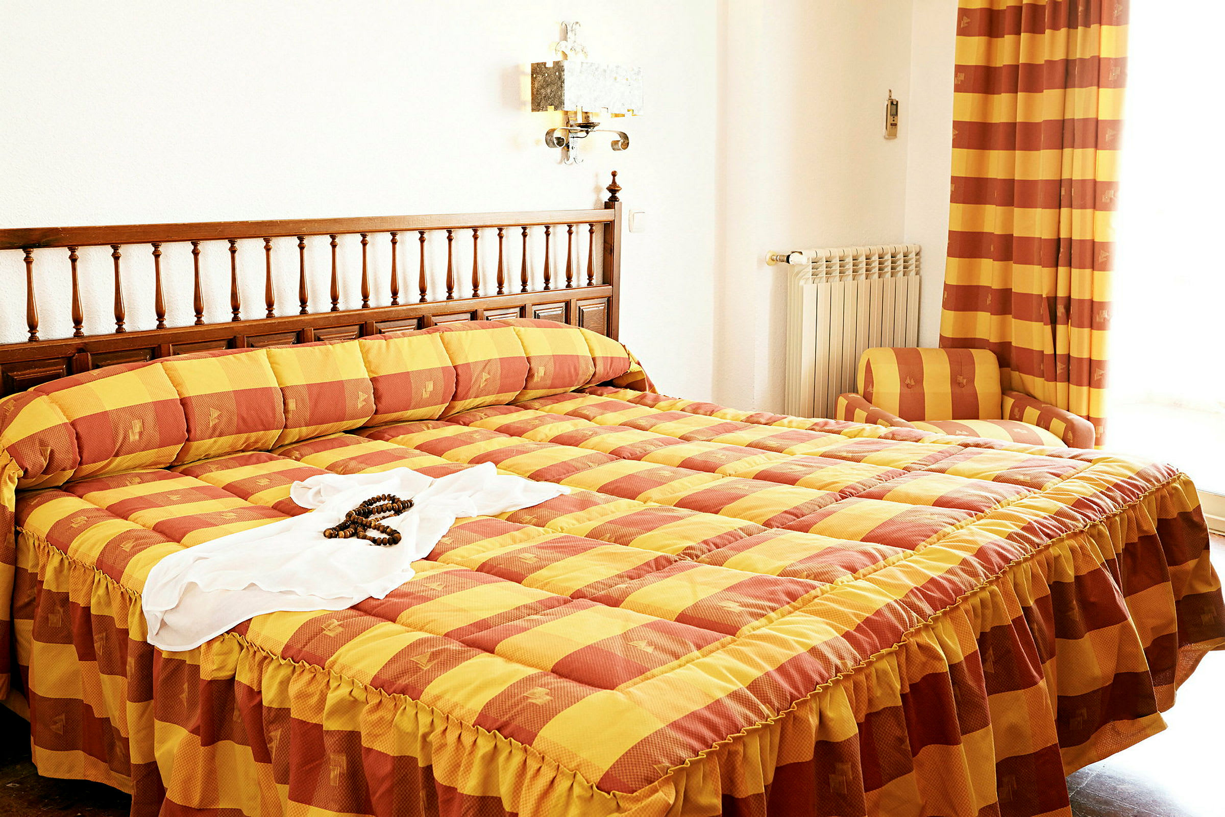 Ett hotellrum med en säng med gul och orange rutigt överkast. (AI-genererad text)