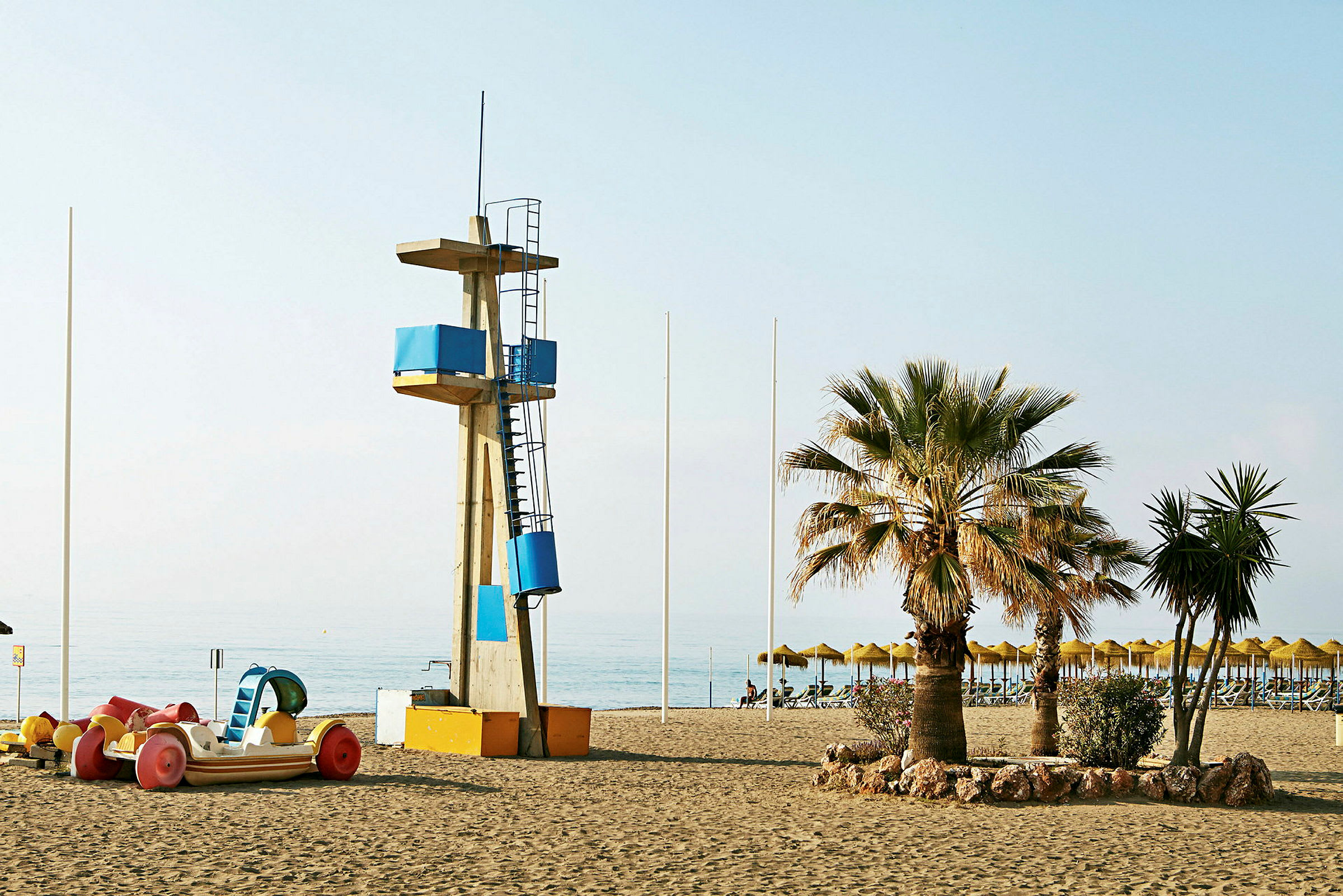 Strand med livvakttorn, en palm och hyrcyklar. (AI-genererad text)