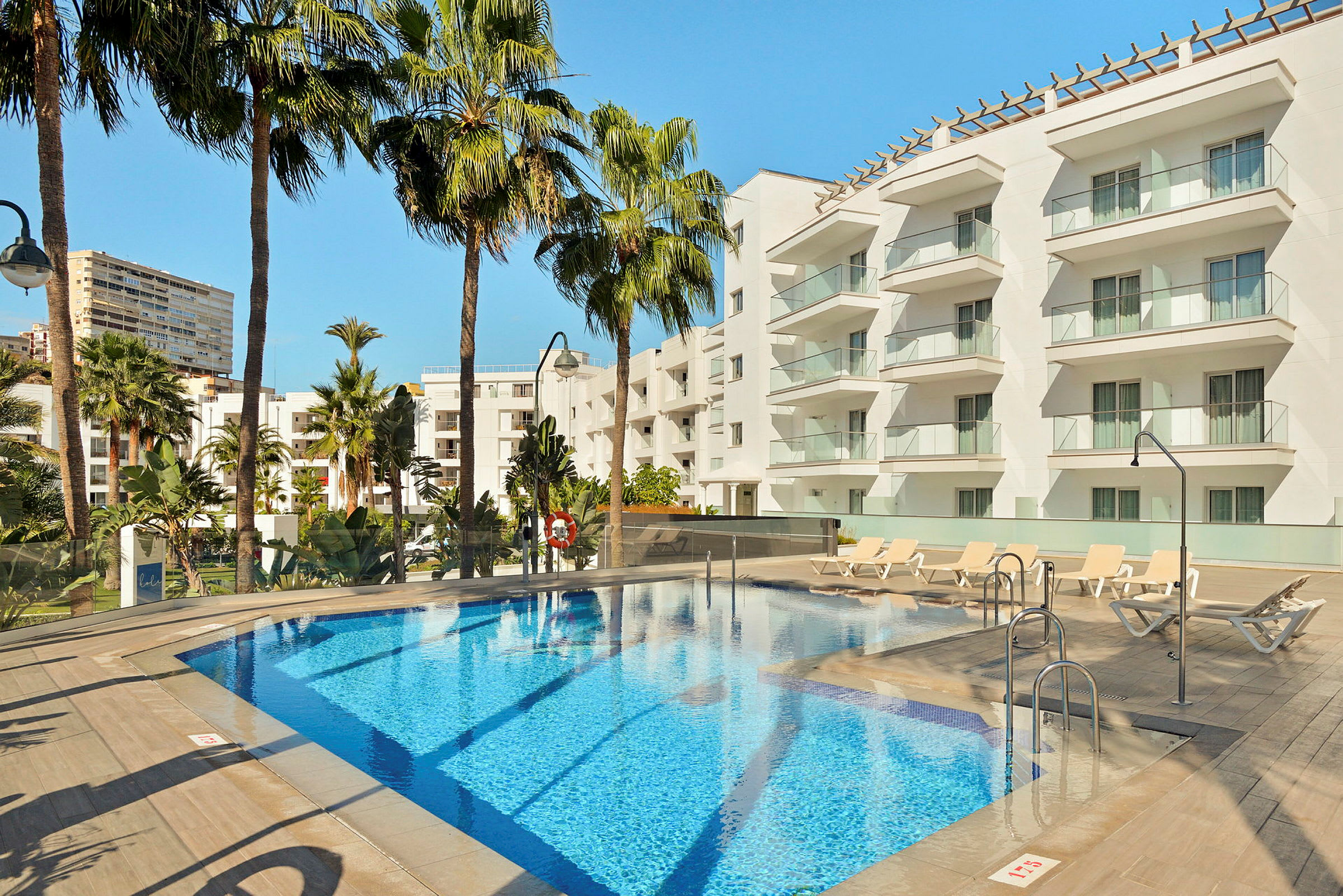 Hotellpool med solstolar och moderna vita byggnader i bakgrunden. (AI-genererad text)