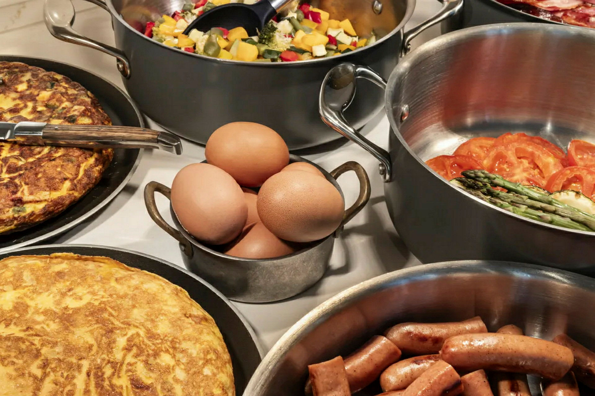 Olika maträtter, inklusive omelett, korv, ägg och grönsaker, arrangerade på ett bord. (AI-genererad text)