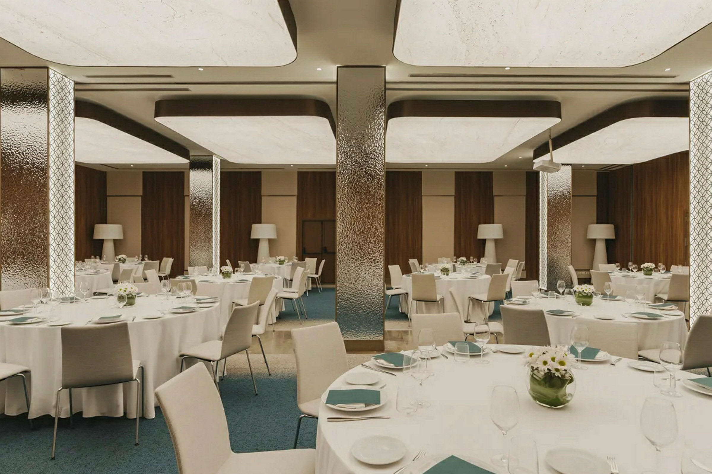 En elegant matsal med dukade runda bord, dekorerade med blommor och serveringsartiklar, omgiven av moderna inredningsdetaljer. (AI-genererad text)
