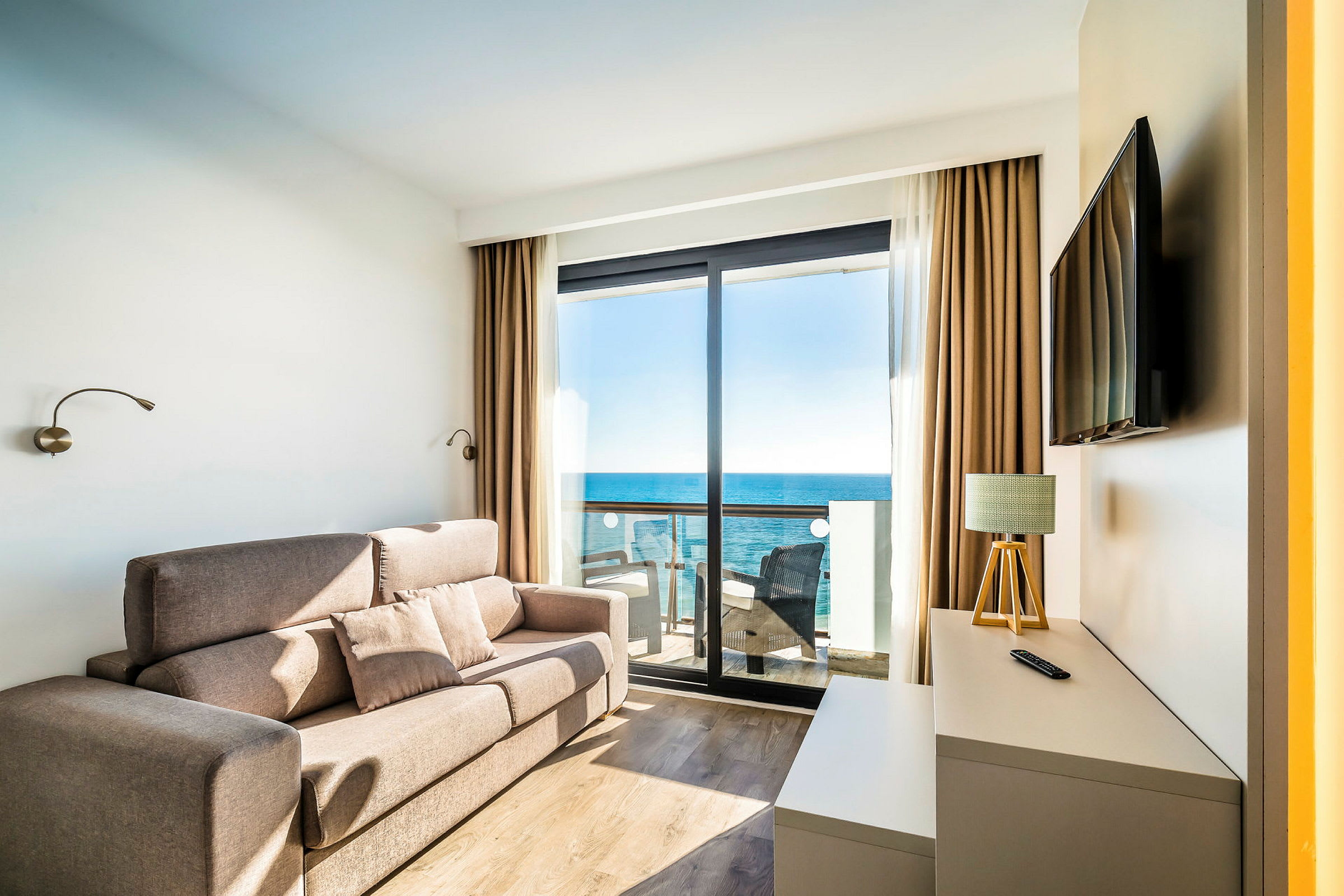 Ett hotellrum med soffa och ett bord framför en balkong med utsikt över havet. (AI-genererad text)
