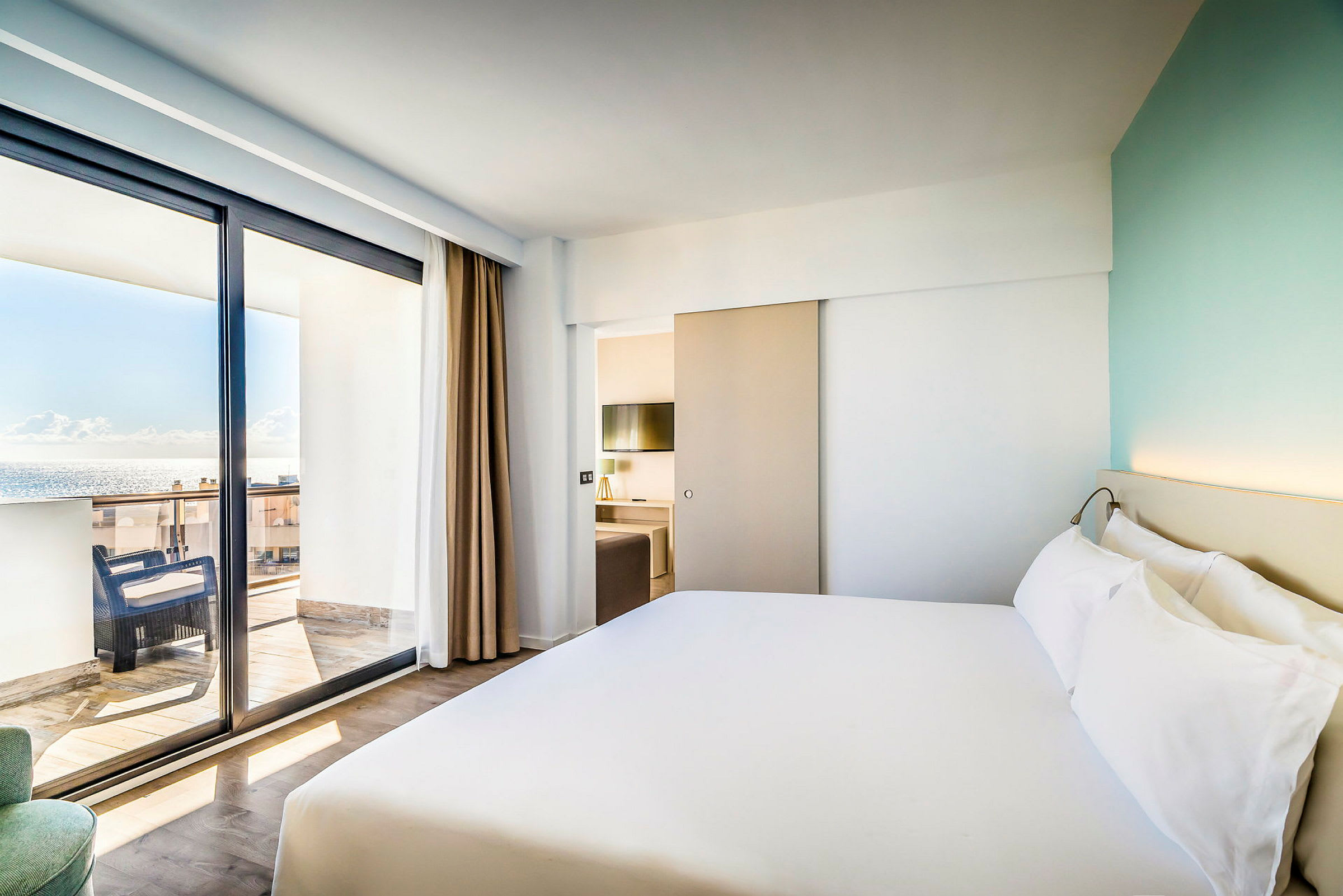 Ett ljust hotellrum med en stor säng och balkong som erbjuder utsikt över havet. (AI-genererad text)