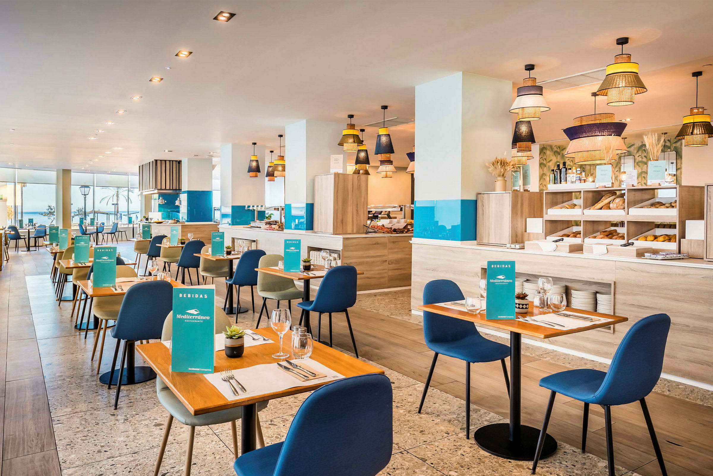 En ljus och modern restaurang med träbord och blå stolar, inredd med dekorativa lampor och ett bufféområde. (AI-genererad text)