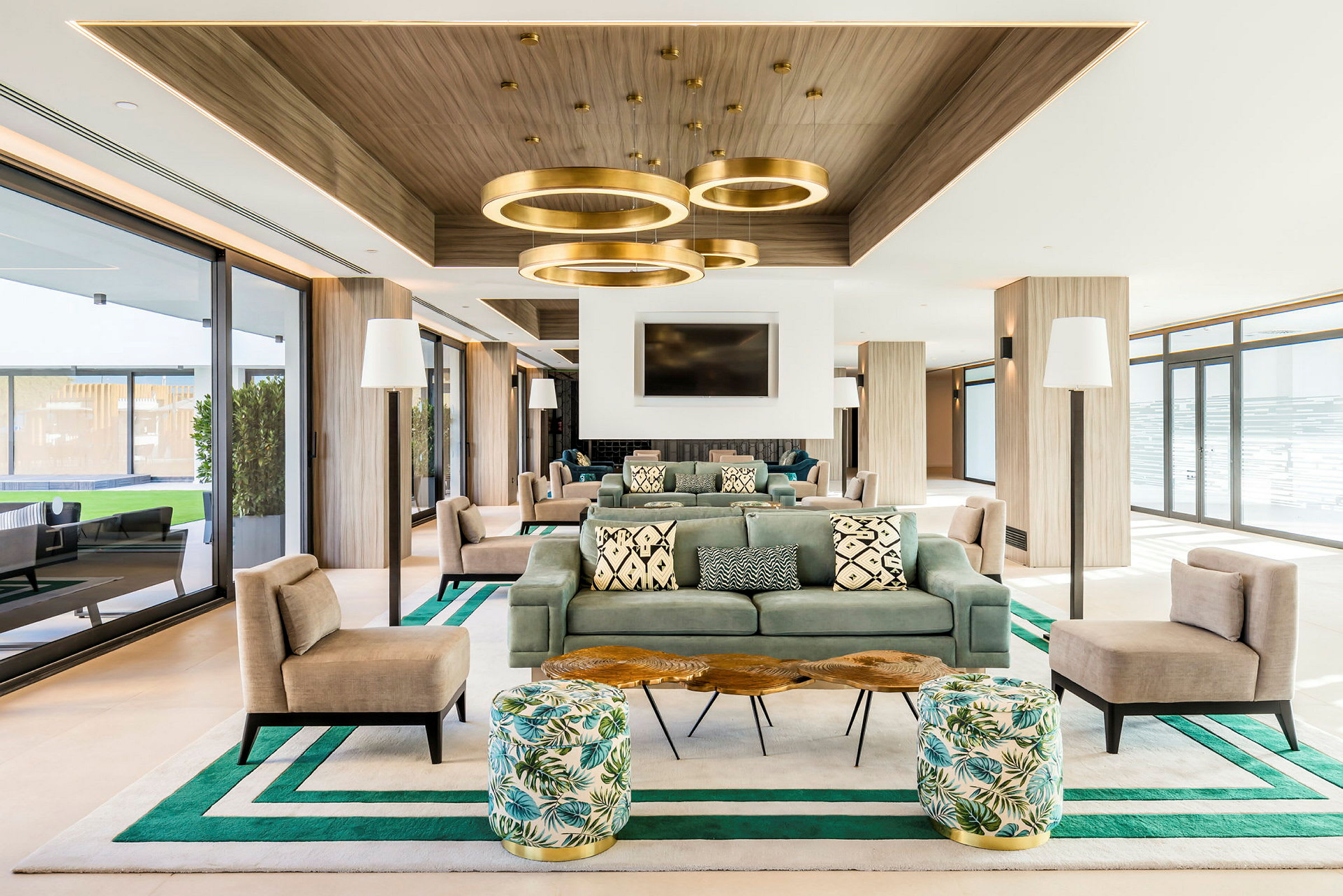 Ett modernt och rymligt vardagsrum med soffor, stolar och dekorativa belysningar. Designade detaljer såsom mönstrade kuddar och gröna accenter skapar en harmonisk atmosfär. (AI-genererad text)