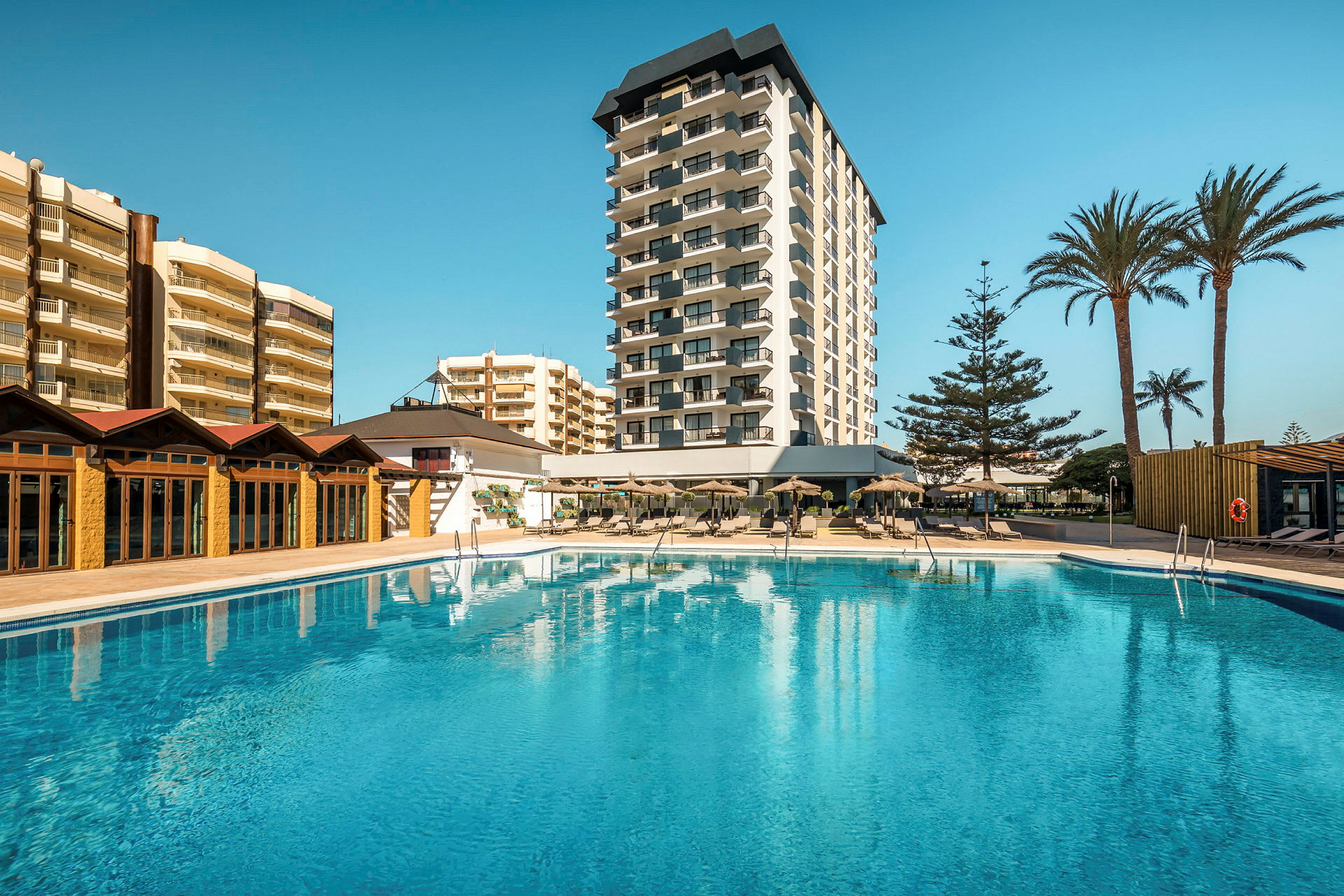 Hotellbyggnad med pool i förgrunden. (AI-genererad text)