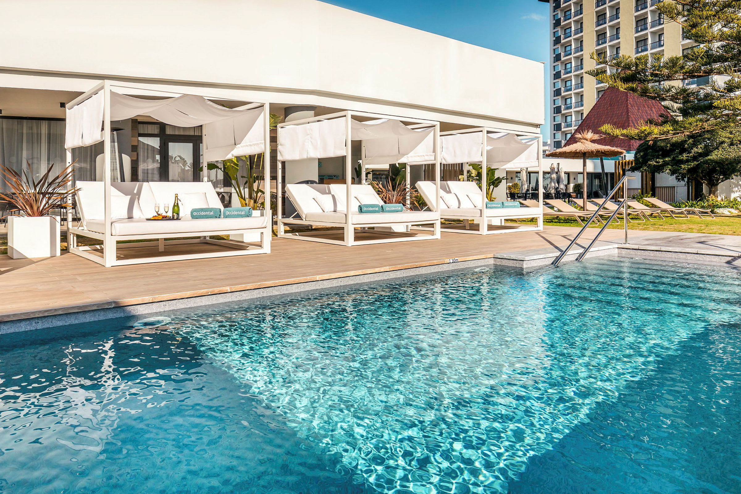 En pool med sittplatser under vita solskydd i bakgrunden. (AI-genererad text)