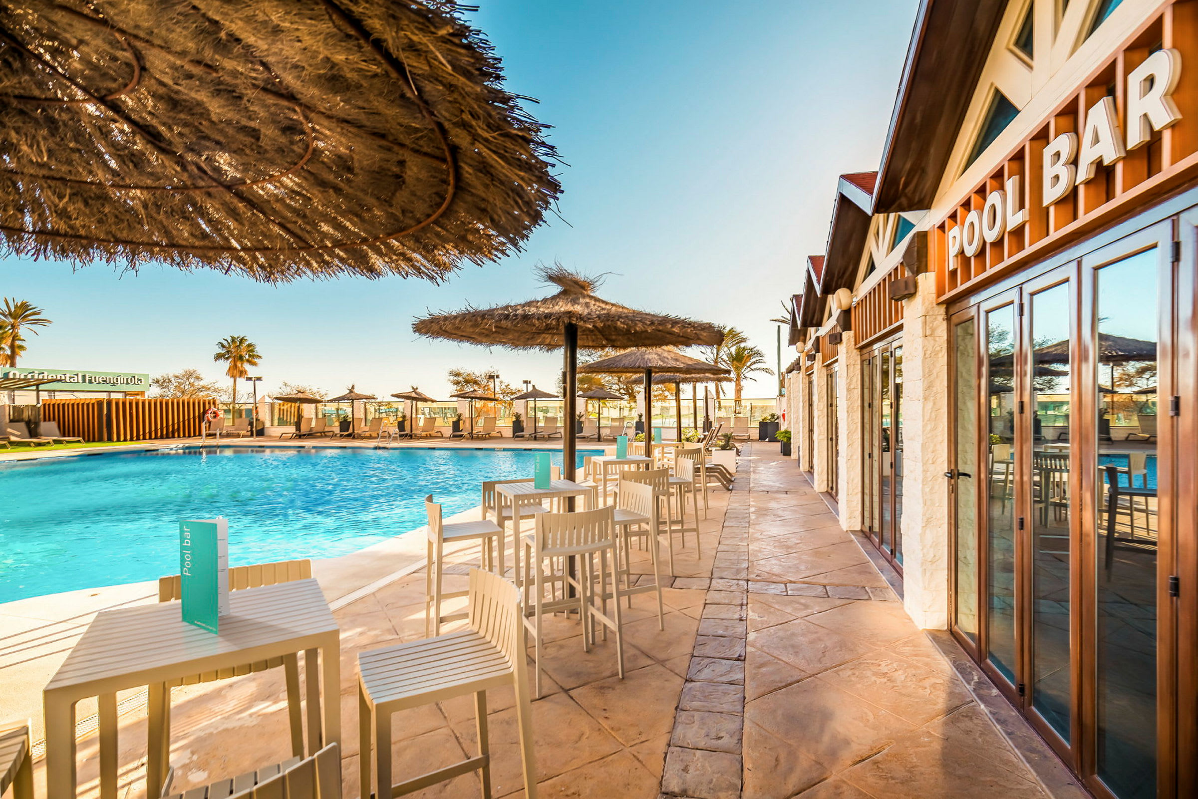 En utomhuspool med parasoller och sittgrupper bredvid en poolbar. (AI-genererad text)