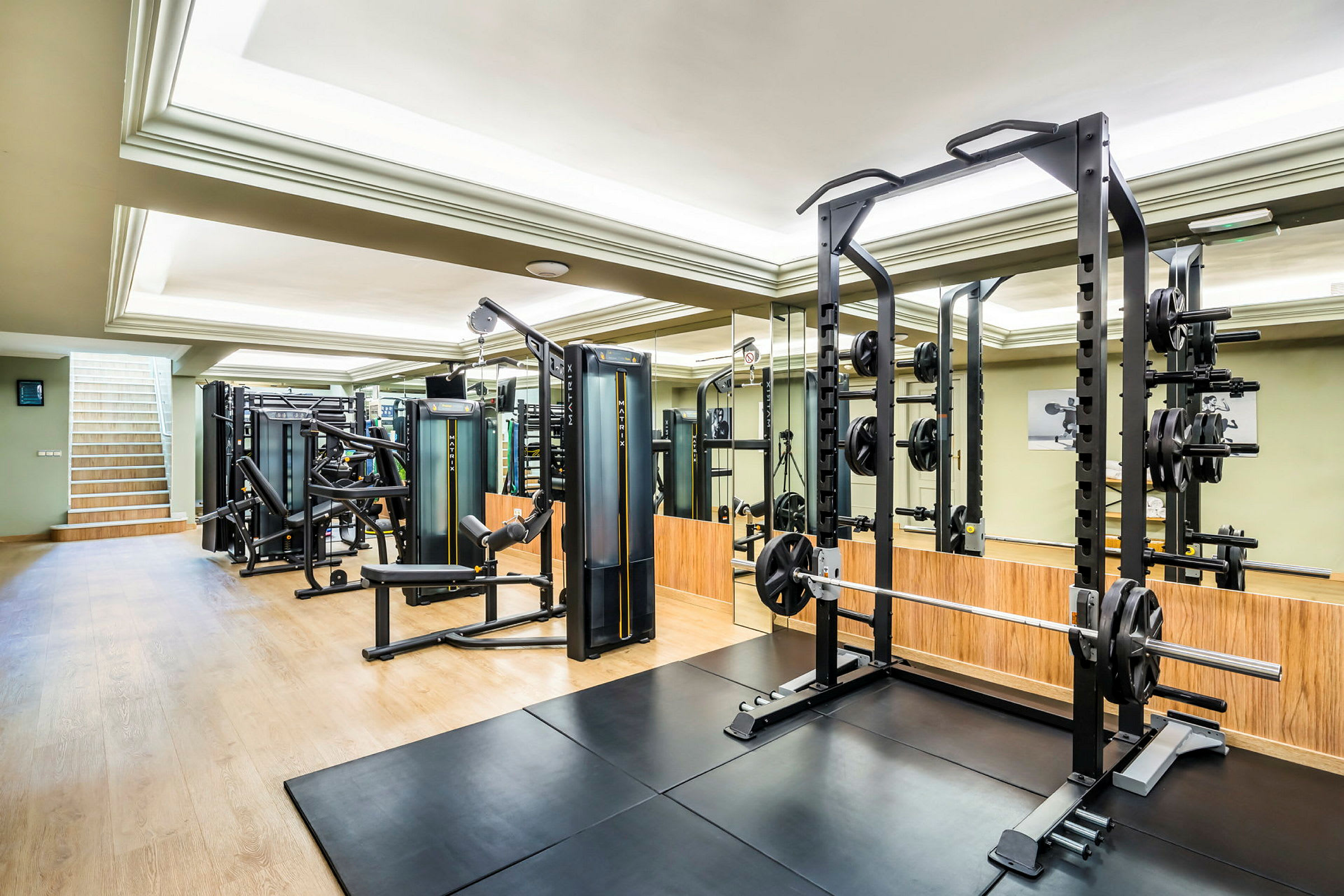 Ett modernt gym med träningsutrustning såsom hantlar och maskiner, speglar på väggarna och trägolv. (AI-genererad text)