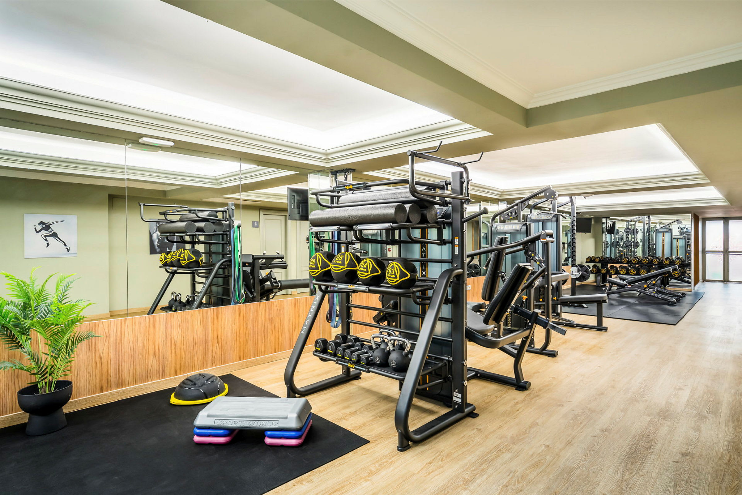 Ett gym med träningsutrustning som fria vikter, maskiner och stepbrädor, samt speglar i bakgrunden. (AI-genererad text)