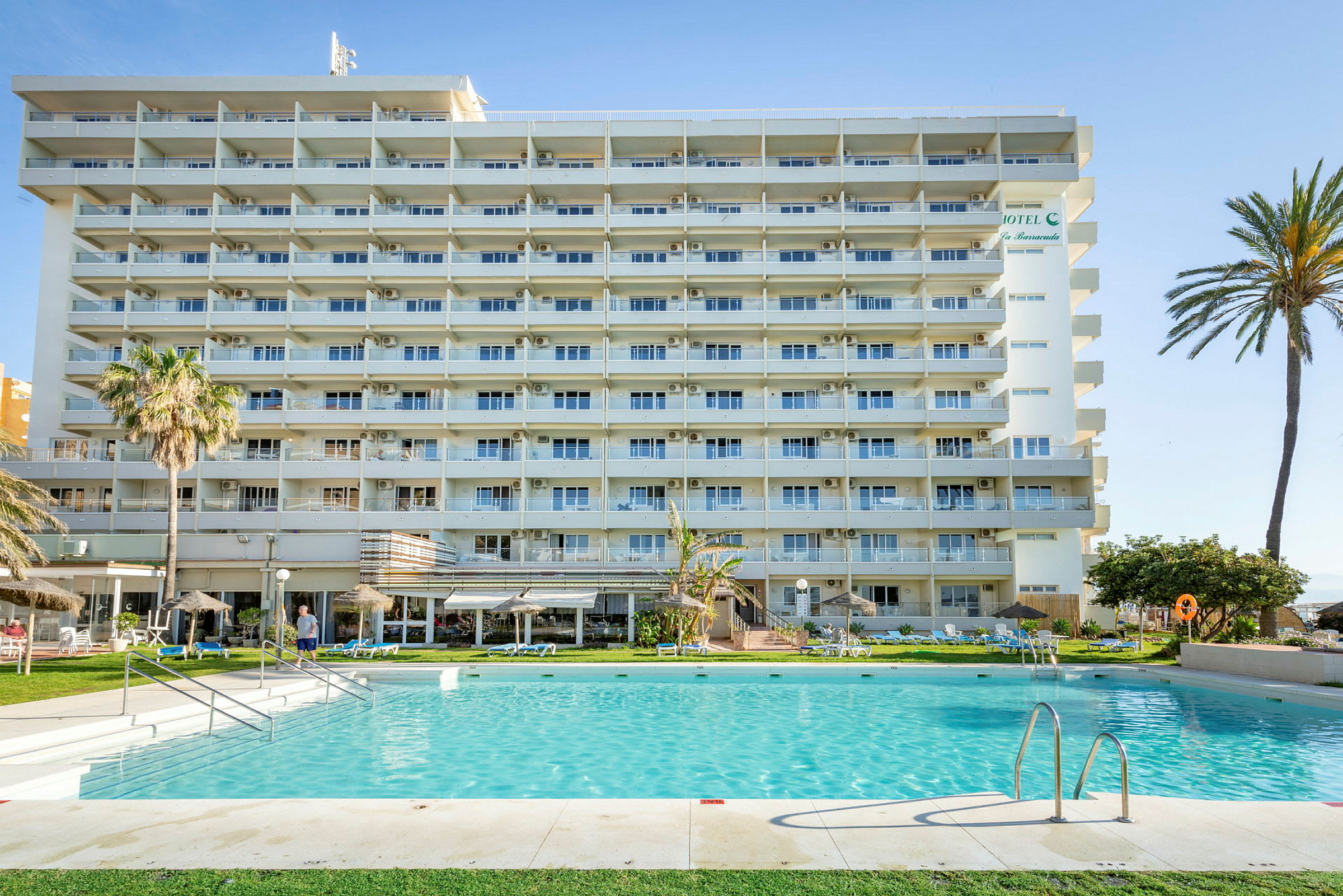 Ett flerbostadshotell med balkonger framför en swimmingpool och omgivande trädgård. (AI-genererad text)