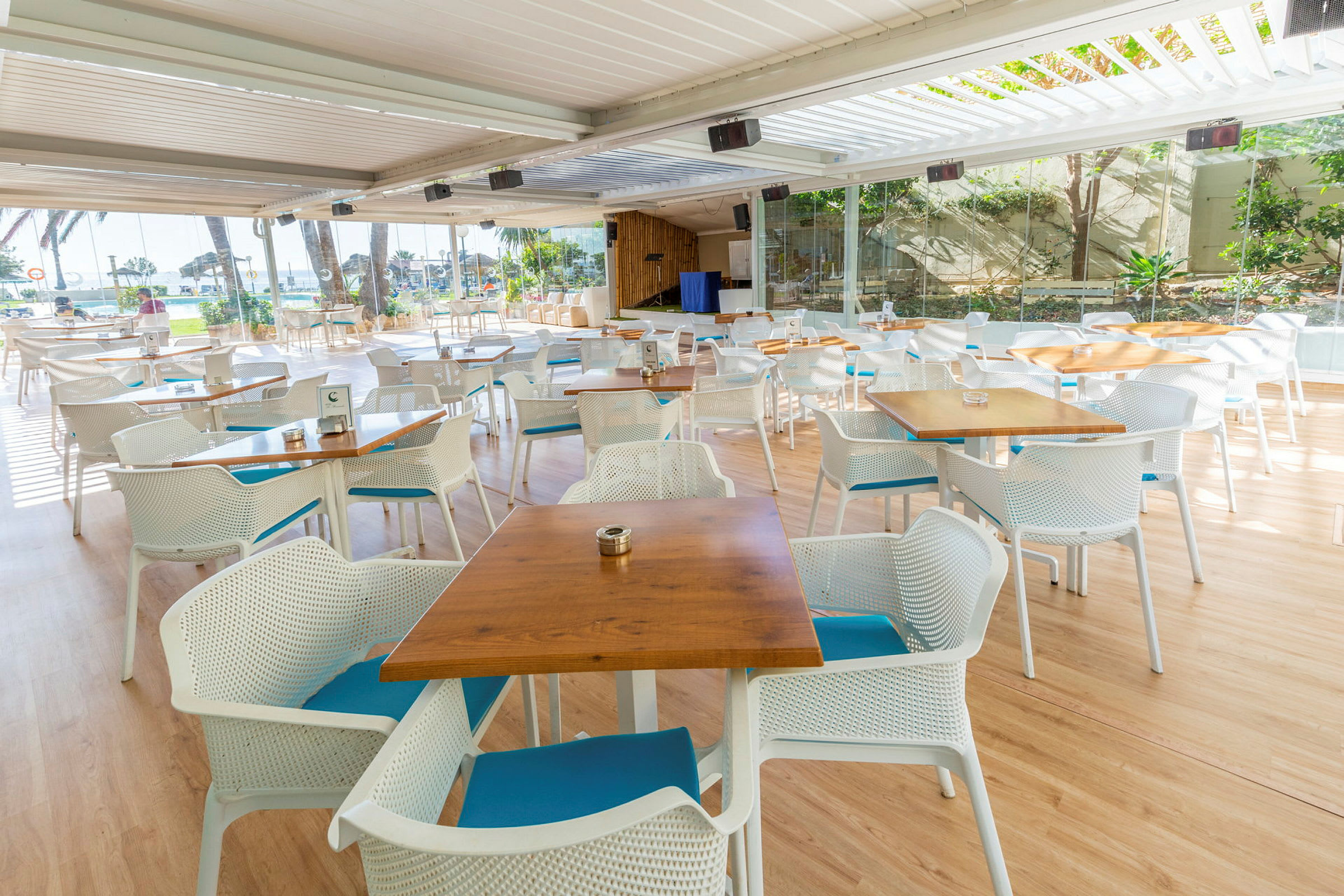 Utomhusrestaurang med bord och stolar framför panoramafönster. (AI-genererad text)