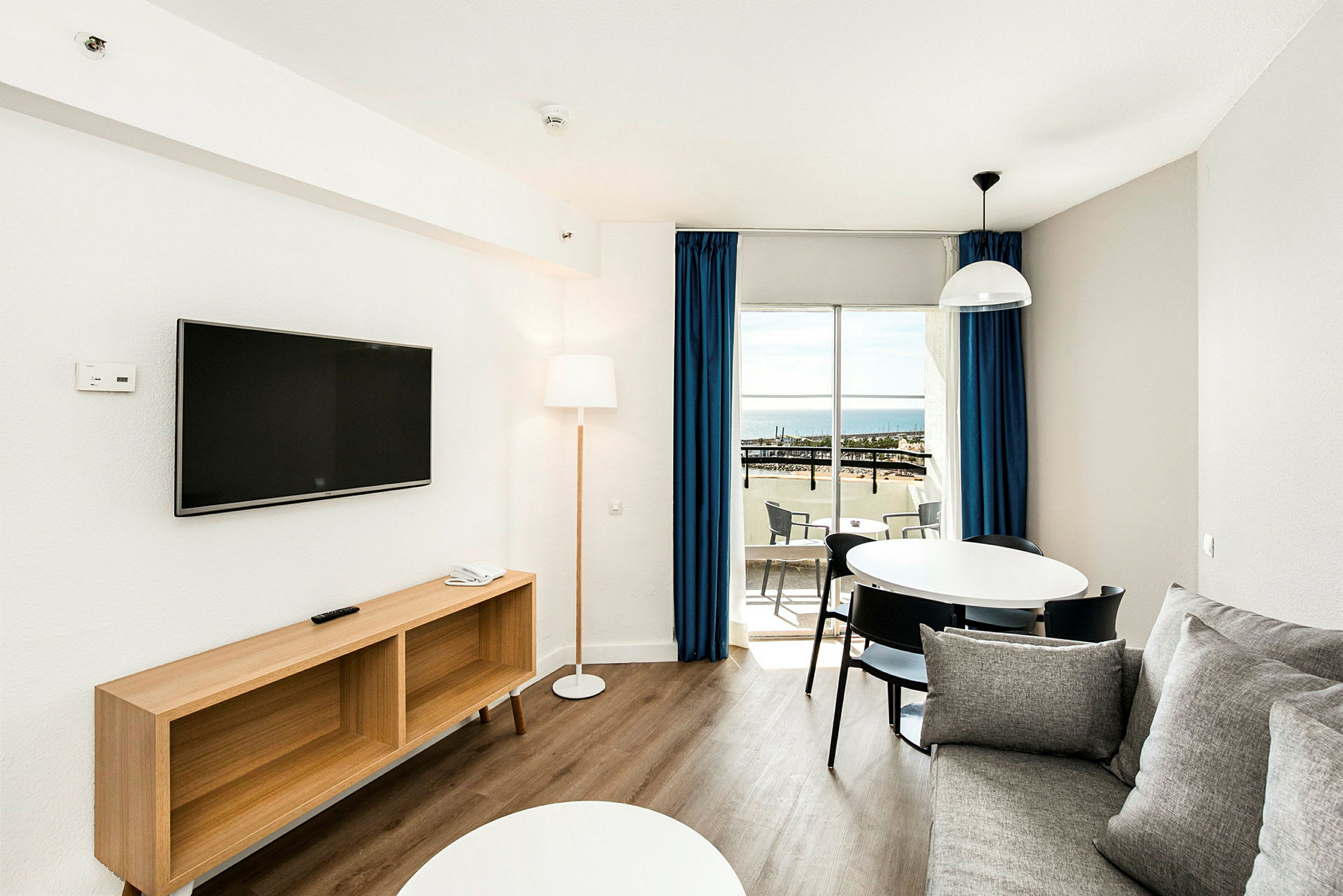 Ett modernt vardagsrum med en soffa, TV, matbord och balkong med havsutsikt. (AI-genererad text)