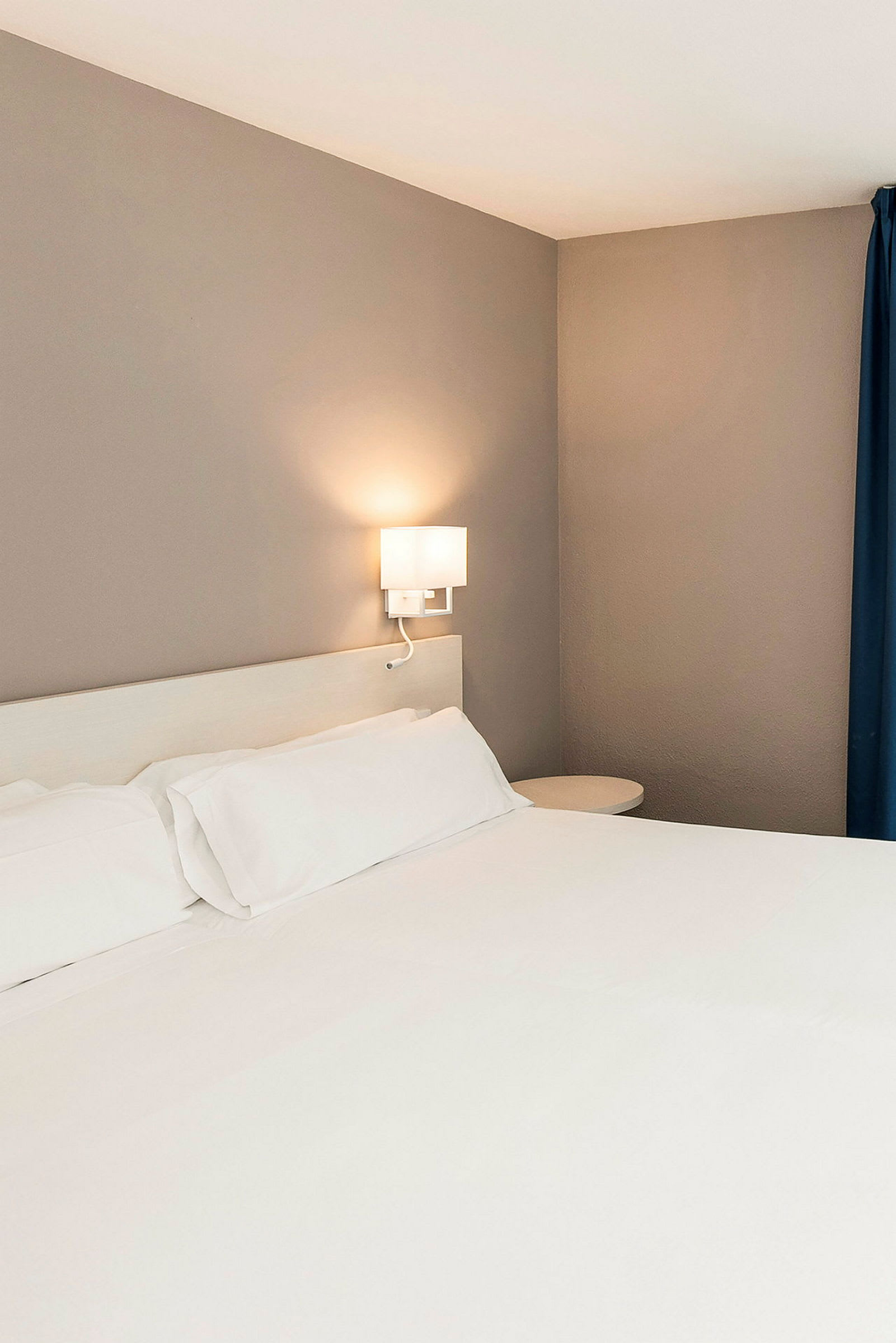 En hotellrumssäng med vita lakan och vägglampa. (AI-genererad text)