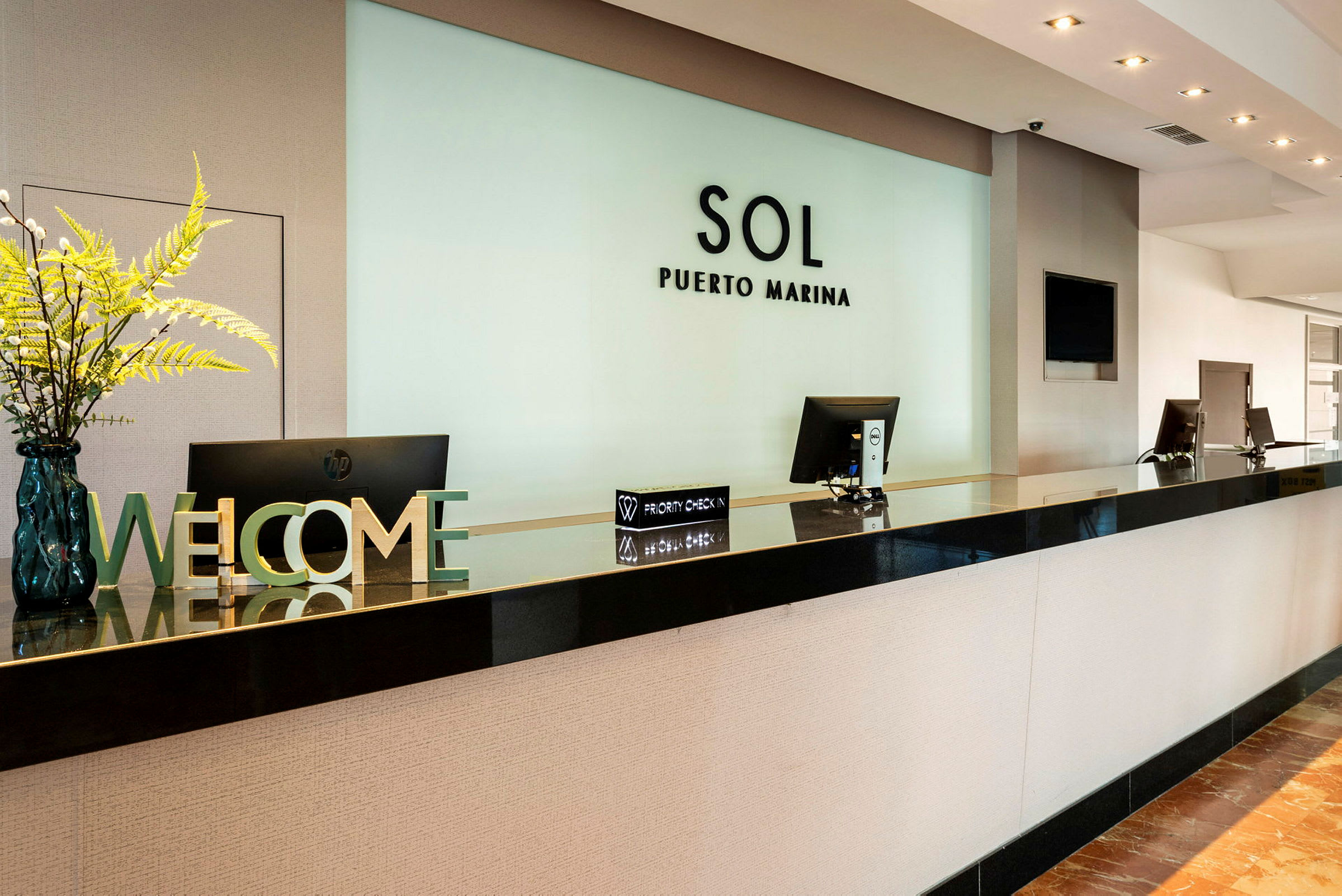 Receptionen på Sol Puerto Marina med datorskärmar och dekorationer, inklusive en välkomstskylt och blomsterarrangemang. (AI-genererad text)