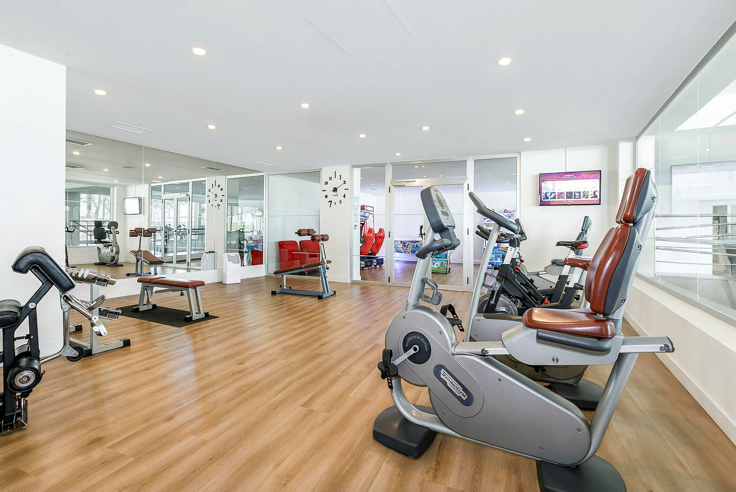 Ett gym med träningsmaskiner och redskap på ett trägolv. Speglar täcker en vägg. (AI-genererad text)