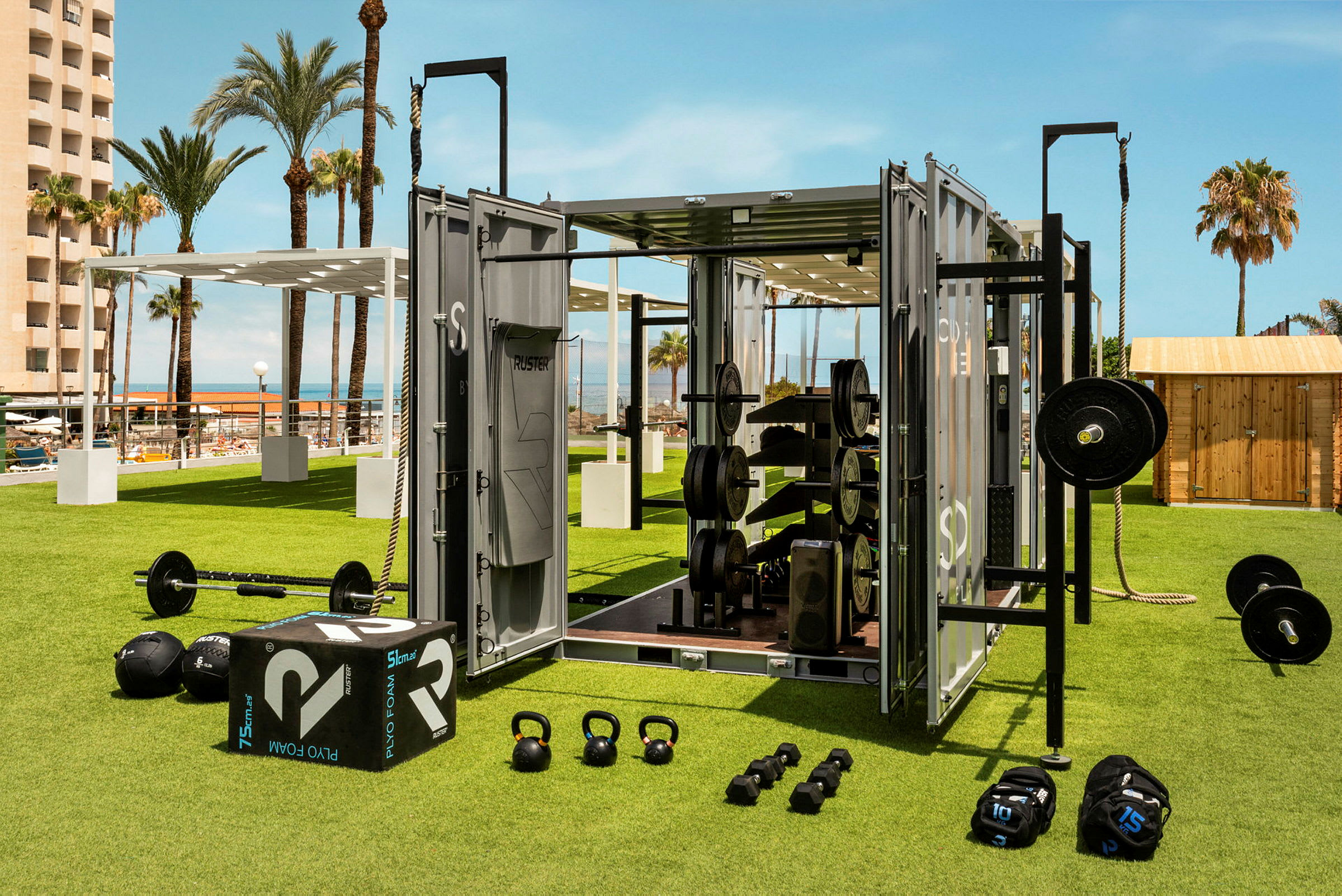 Utomhusgym med träningsutrustning på en gräsyta med soligt väder och palmer i bakgrunden. (AI-genererad text)