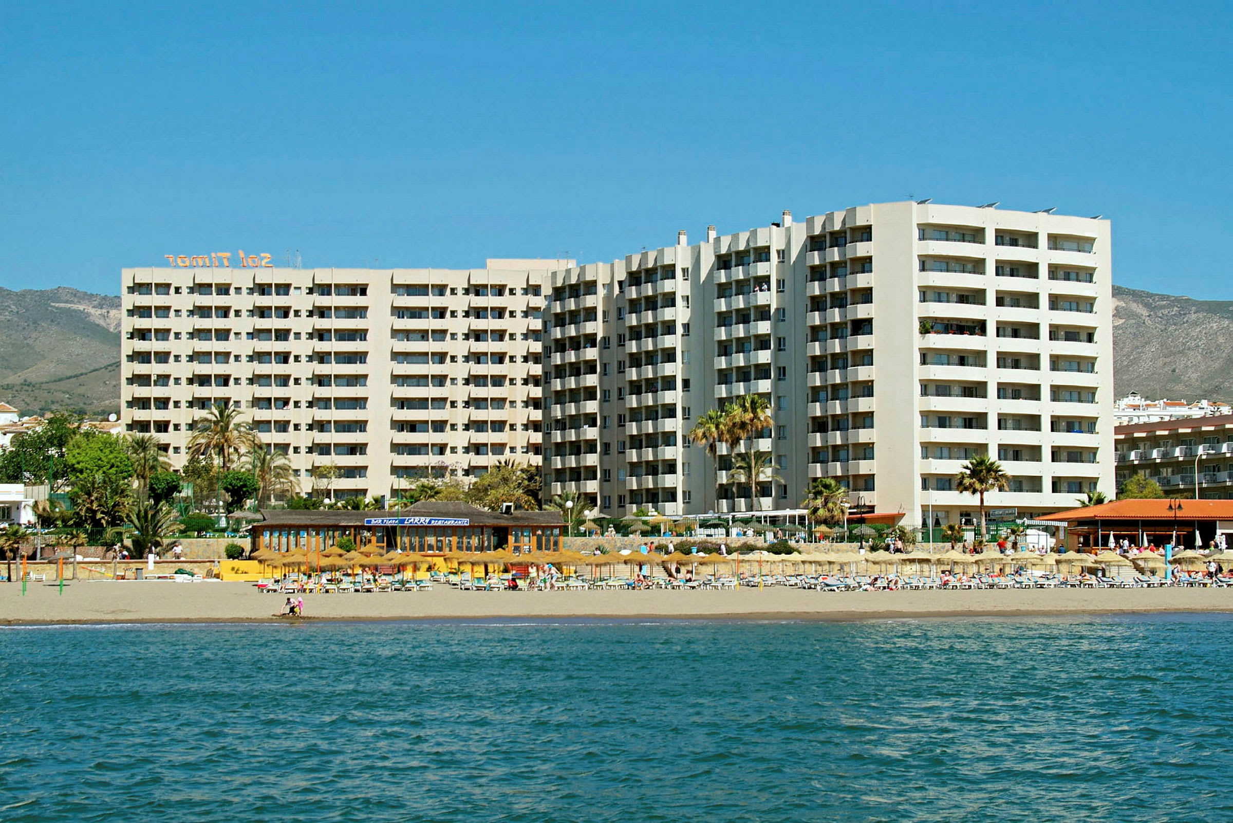 Strandhotell med höga byggnader och solstolar vid vattnet. (AI-genererad text)