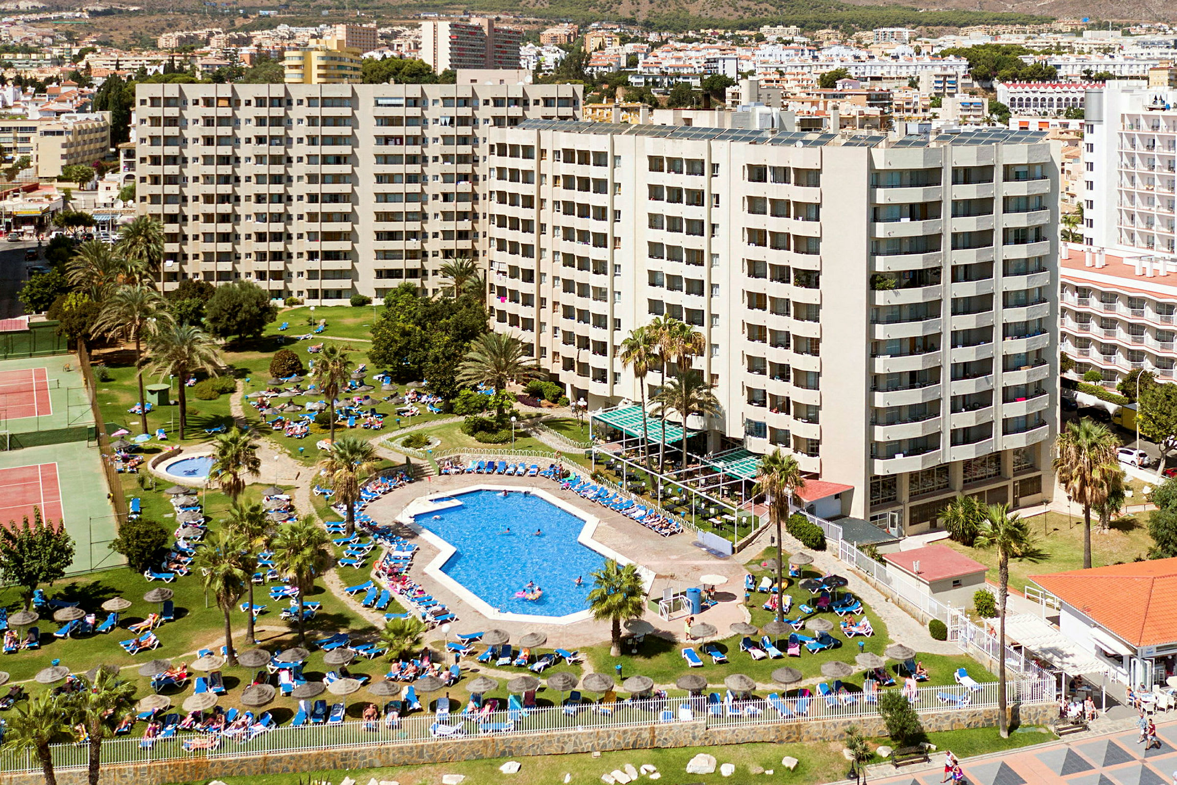 Översiktsbild av hotellområde med pool, palmträd och grönområde. (AI-genererad text)