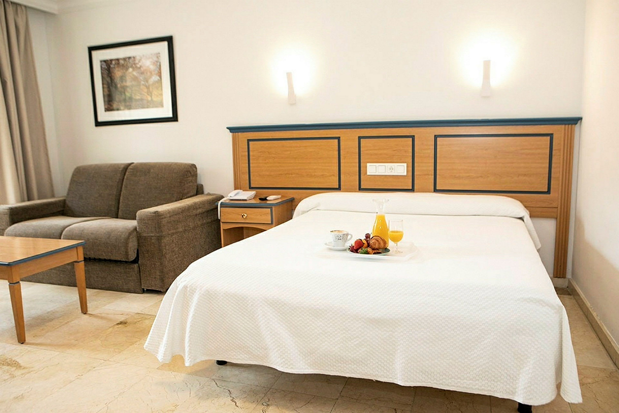 Hotellrum med bäddad säng och soffa. (AI-genererad text)