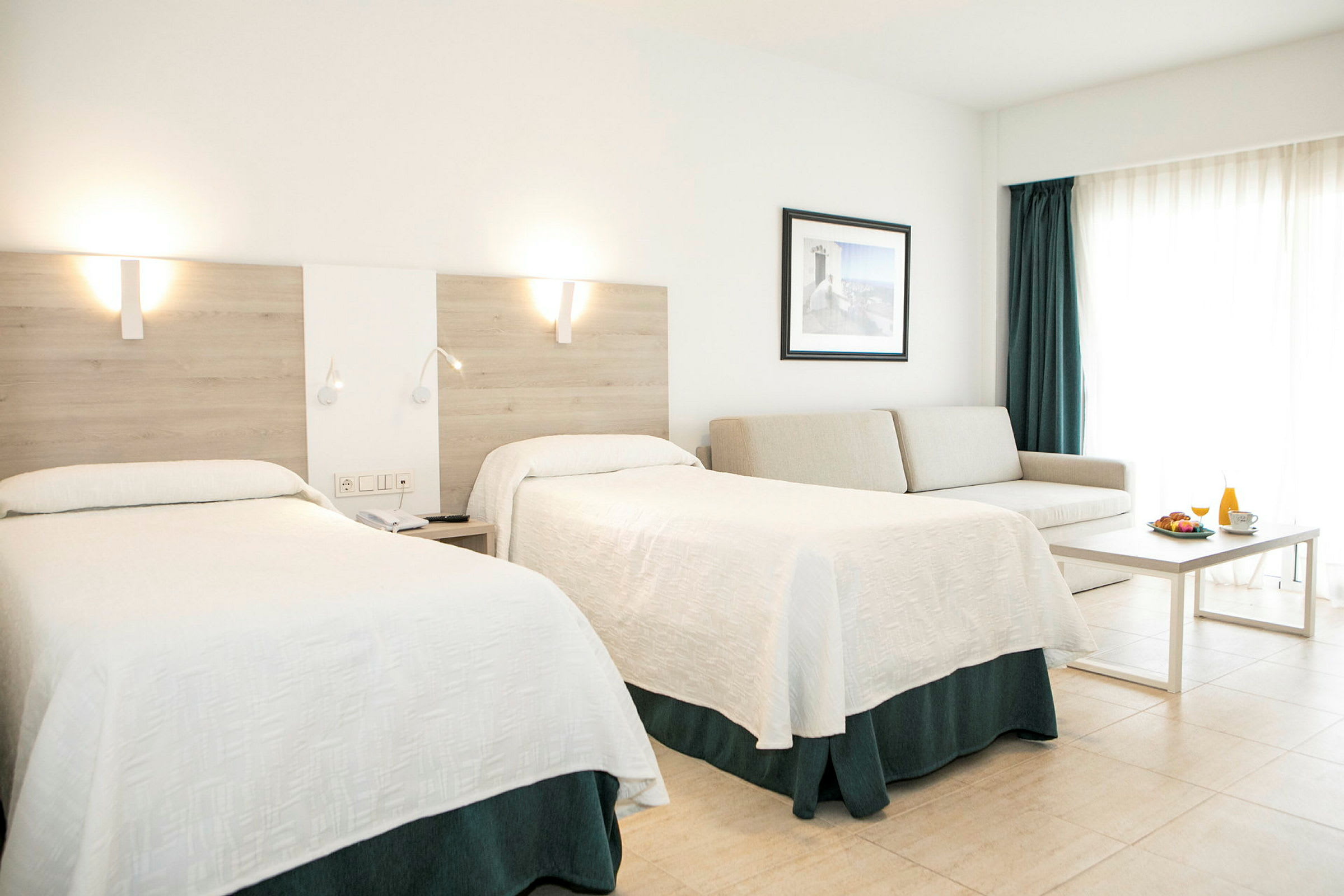 Ett hotellrum med två sängar, en soffa, ett bord och en frukostservering. (AI-genererad text)