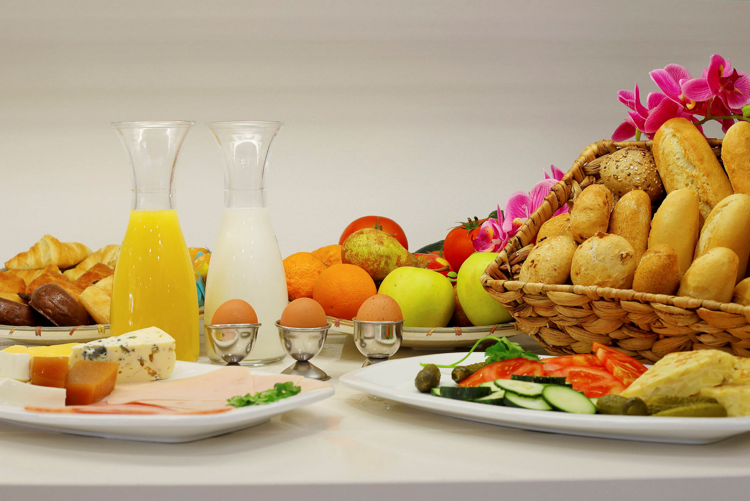 En frukostbuffé med olika bröd, frukt, grönsaker, ost, kallskuret, kokta ägg samt drycker som juice och mjölk. (AI-genererad text)