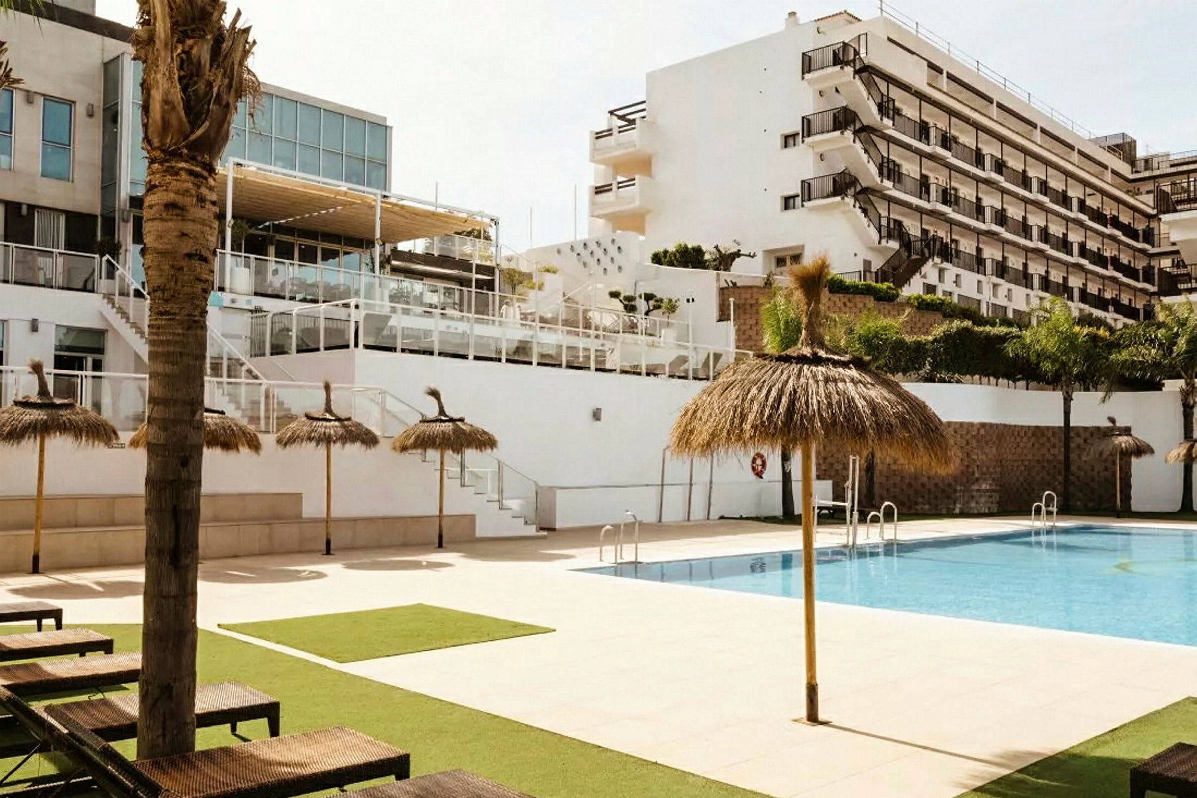 En pool med parasoller och solstolar framför ett fler våningshotell. (AI-genererad text)