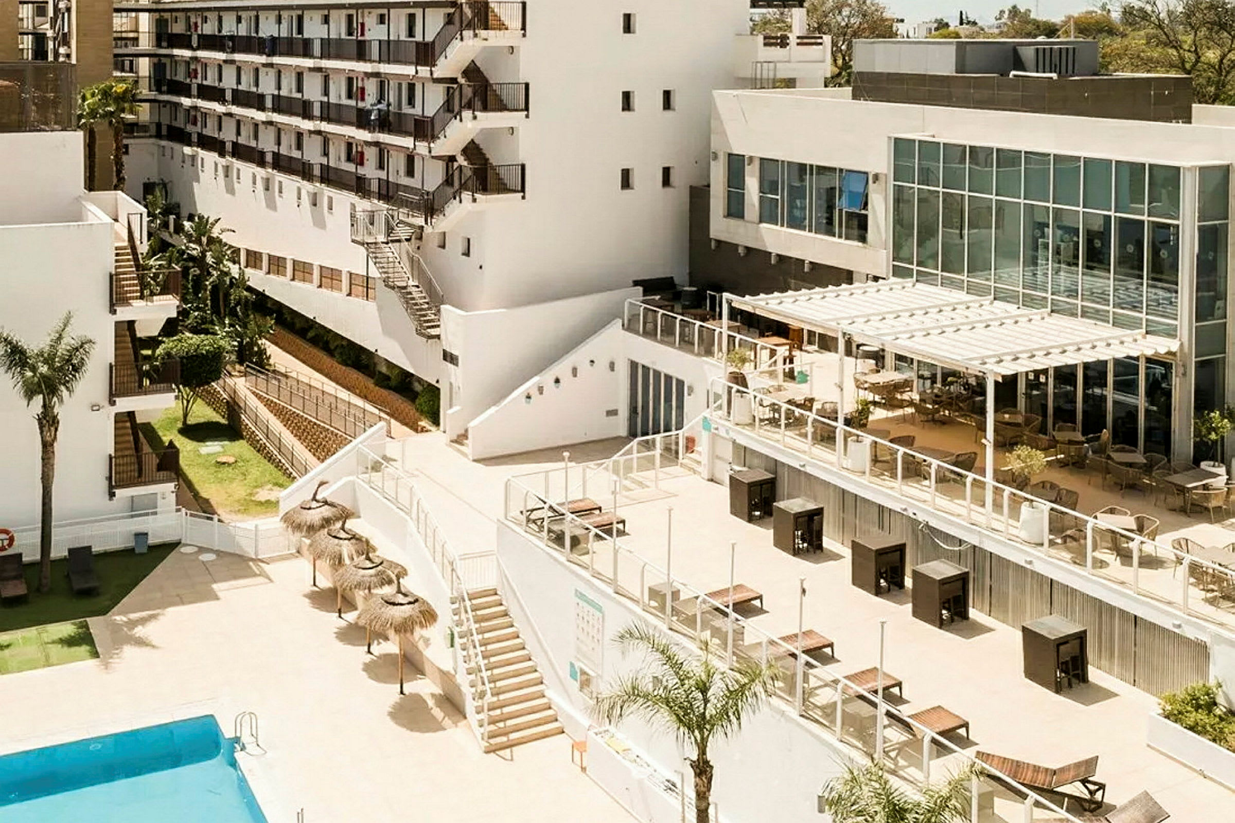 Bild på ett hotellområde med pool, terrass samt vita byggnader. (AI-genererad text)