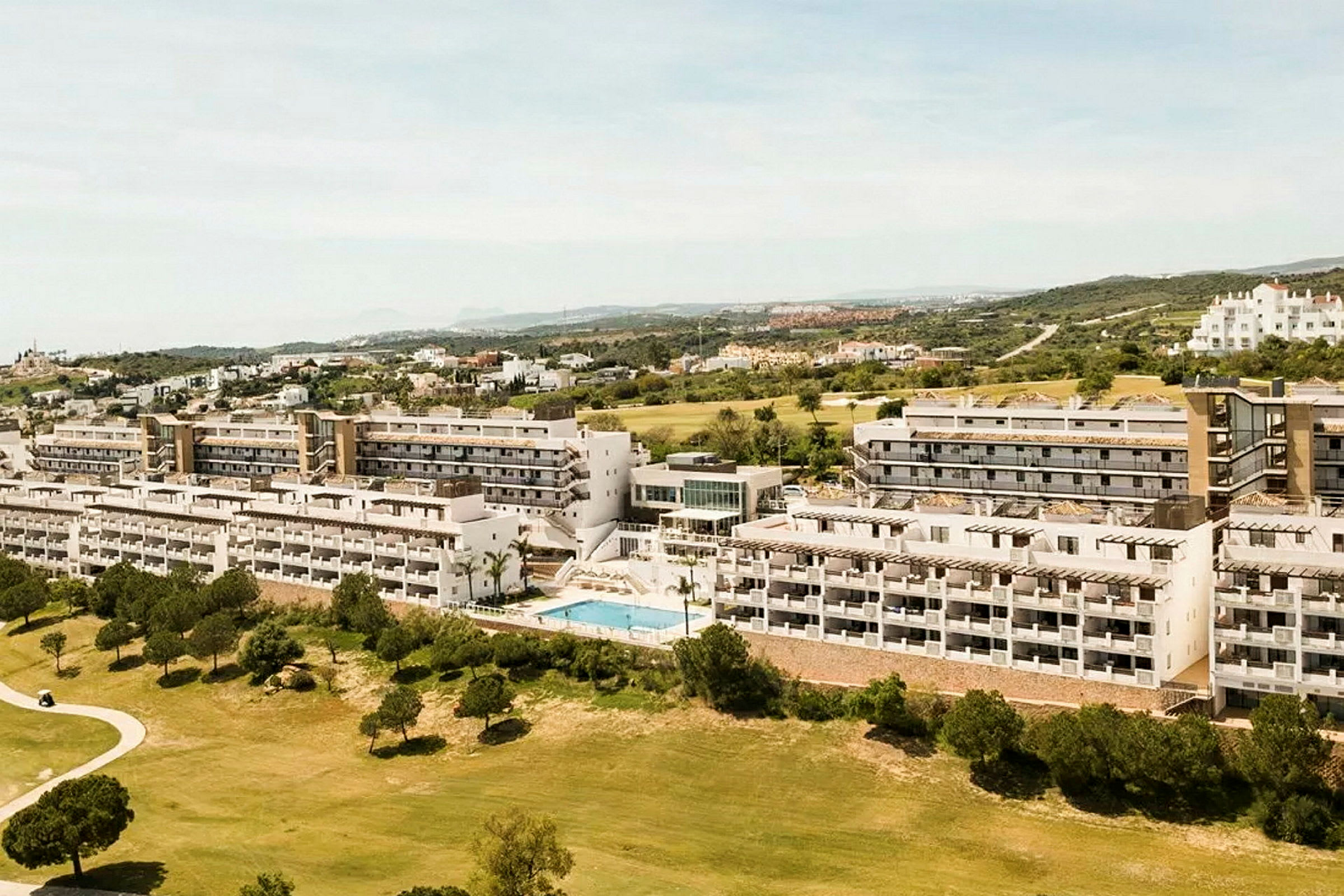 Flygvy av ett hotellområde med flera våningsbyggnader, omgivna av grönska och en pool. (AI-genererad text)