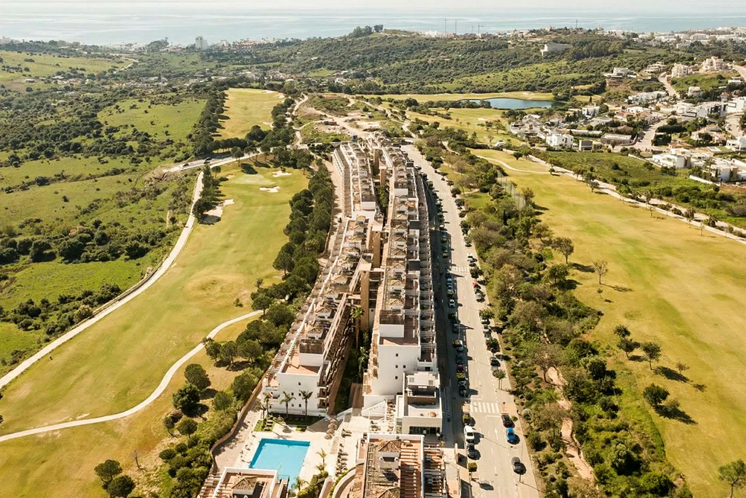 Flygvy över ett bostadskomplex med pool, intill en golfbana och gröna landskap. (AI-genererad text)