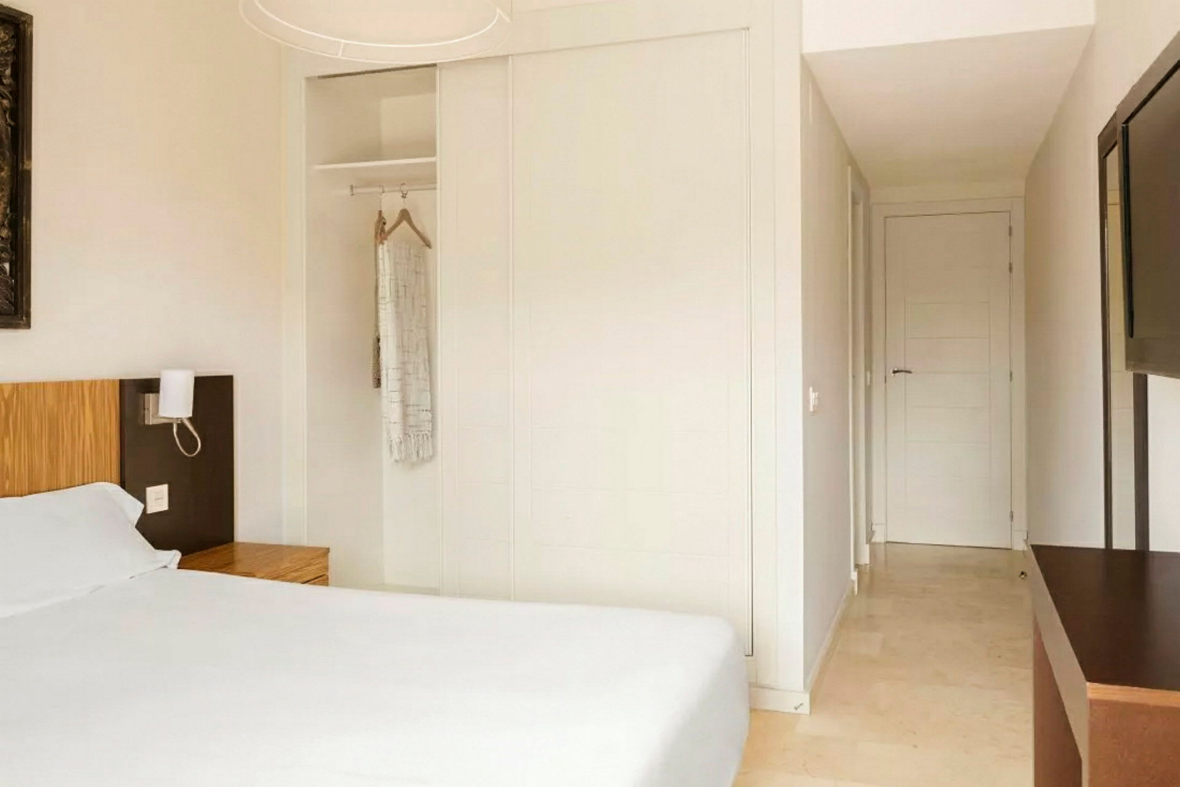 Bild av ett hotellrum med en säng och ett träklädställ, en vit garderob och en öppen dörr i bakgrunden. (AI-genererad text)