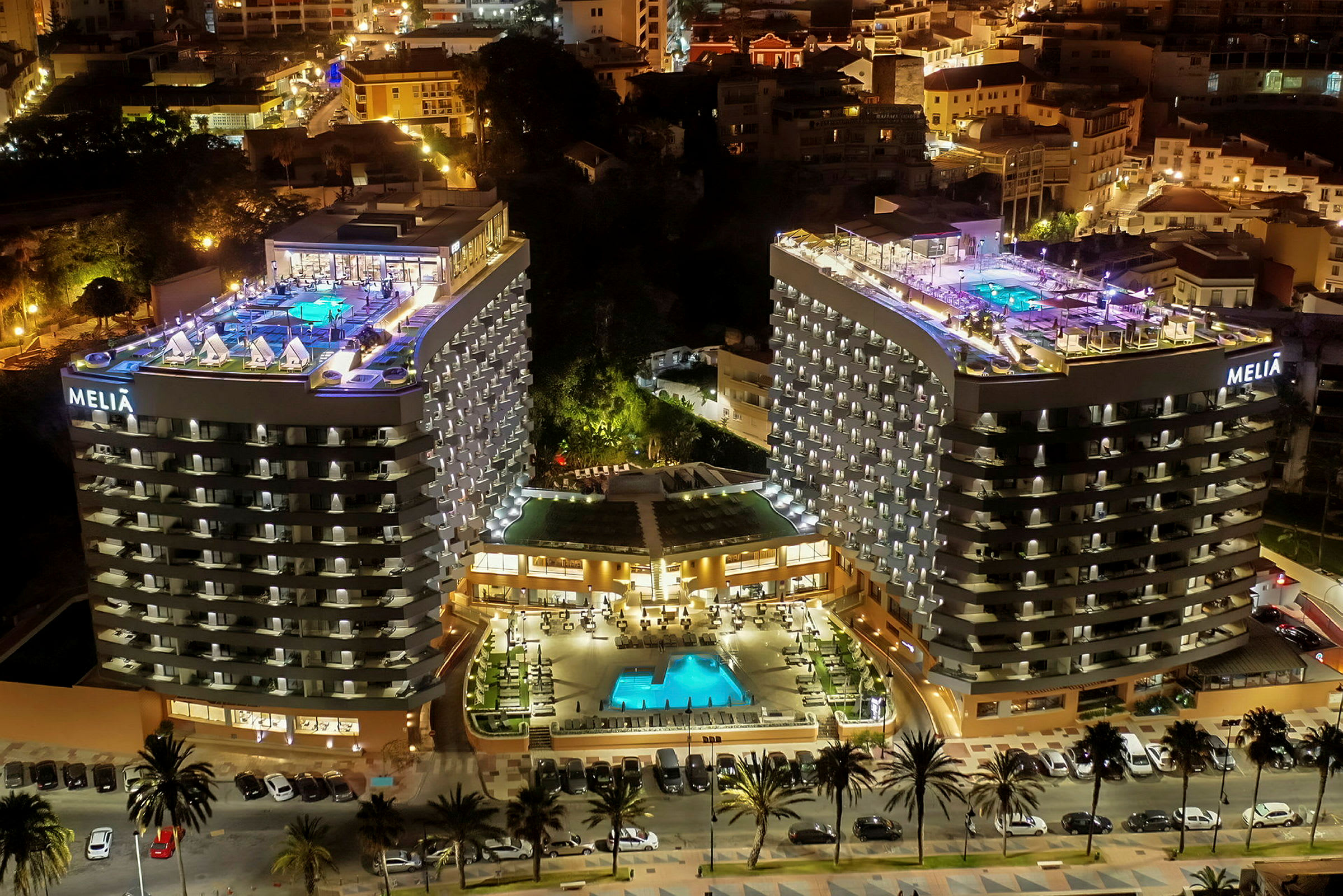 Ett hotellkomplex kvällstid med två höghus, en upplyst pool och terrasser. (AI-genererad text)