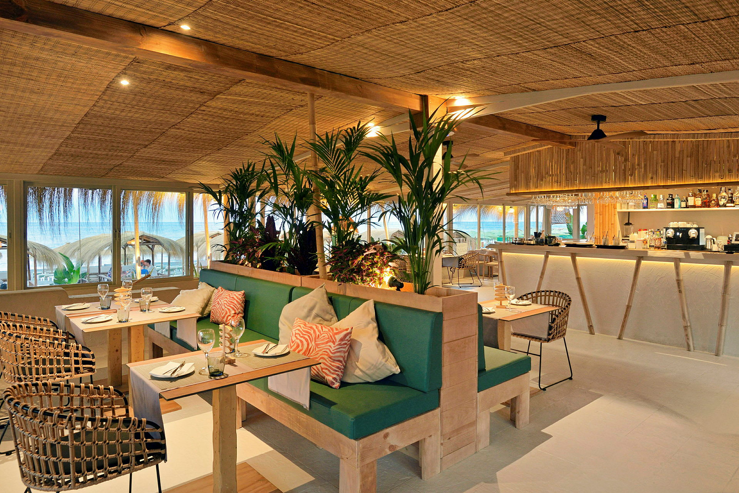 Restaurang med modern inredning, gröna växter och utsikt mot stranden. (AI-genererad text)