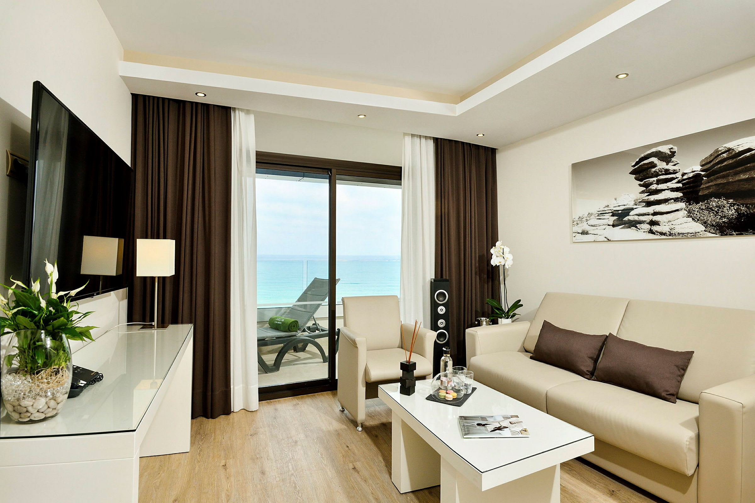 Modernt vardagsrum med beige soffa, soffbord och utsikt över havet genom altandörrar. (AI-genererad text)