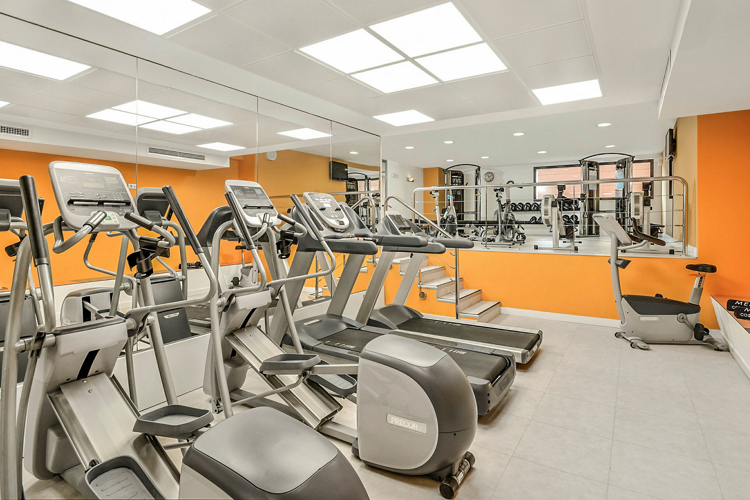 Ett gym med träningsmaskiner, löpband och en orange vägg. (AI-genererad text)