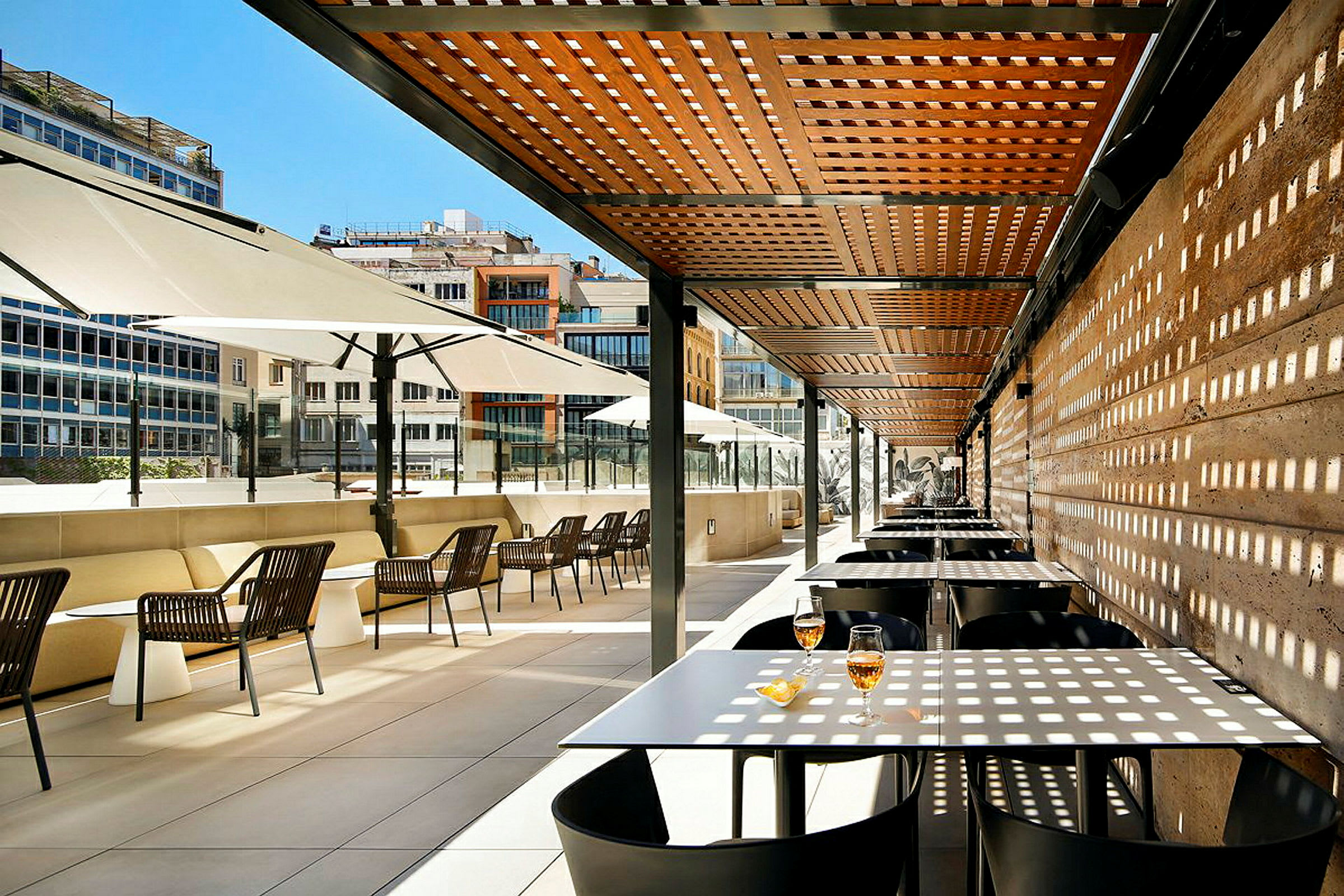 En utomhusterrass med bord och stolar under ett träpergola och stora parasoller. (AI-genererad text)