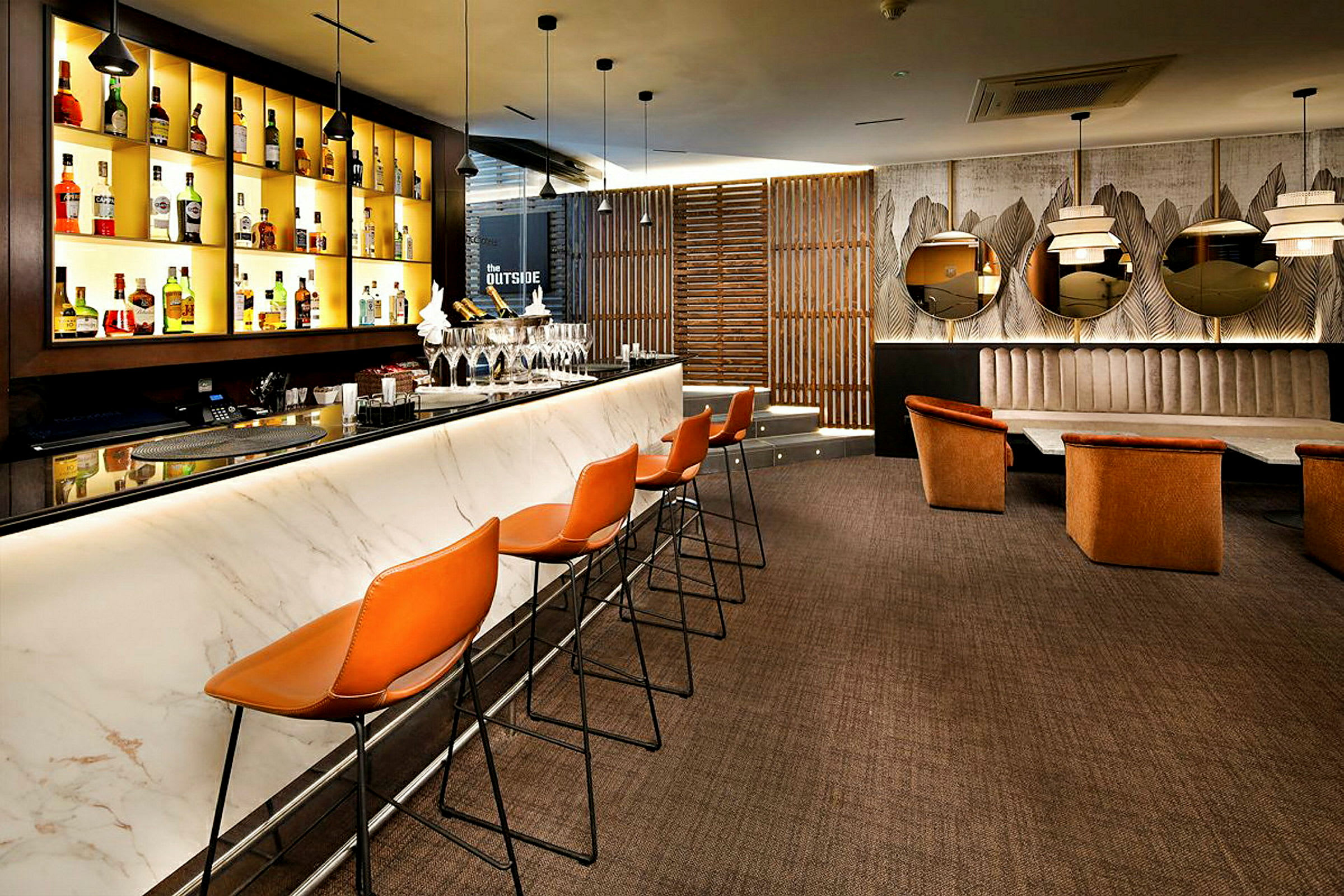 En modern bar med marmordisk, barstolar och hyllor med olika flaskor. I bakgrunden finns sittplatser och dekorativa speglar. (AI-genererad text)