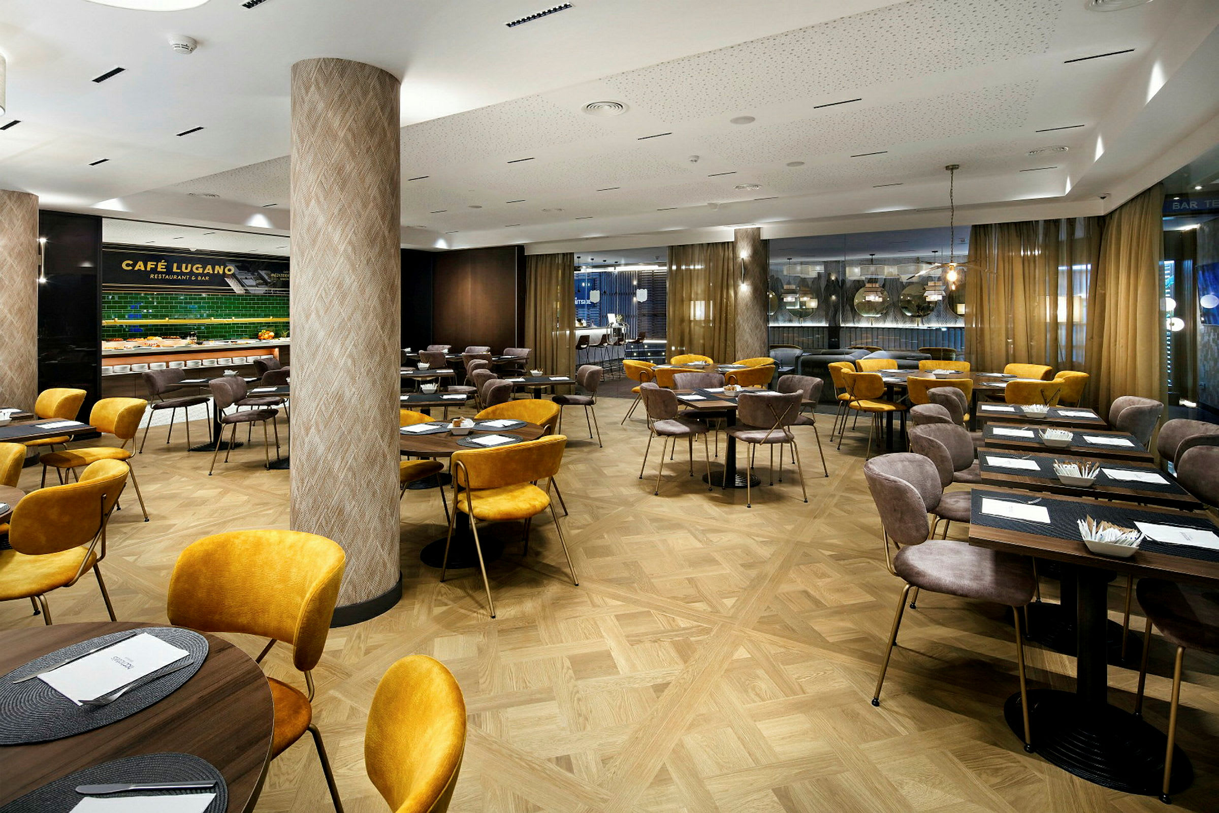 En modern restaurang med bord och stolar i guld och bruna färger, samt stora fönster och dekorativa pelare. (AI-genererad text)