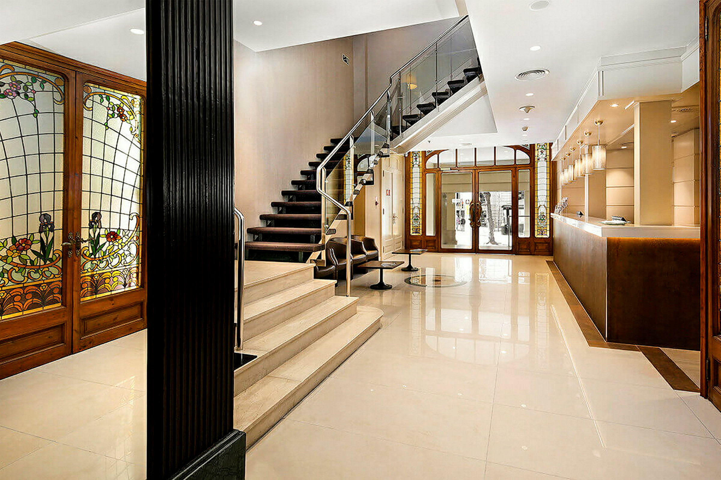 Ett receptionområde med en elegant inredning. Det finns en trappa med en glasräcke, färgglada glasdörrar och en reception med hängande lampor. (AI-genererad text)