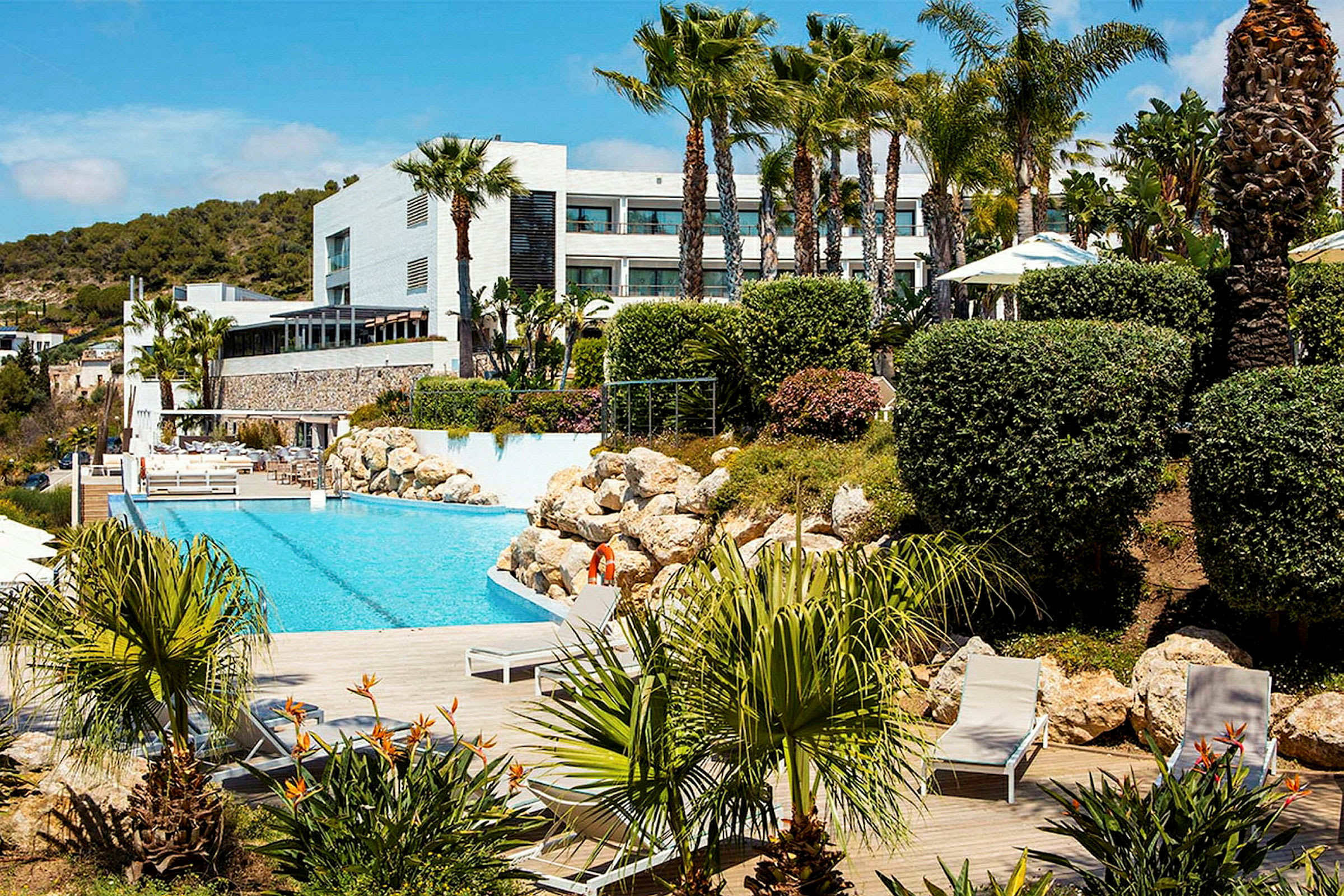 En swimmingpool omgiven av en grönskande trädgård och moderna byggnader. (AI-genererad text)