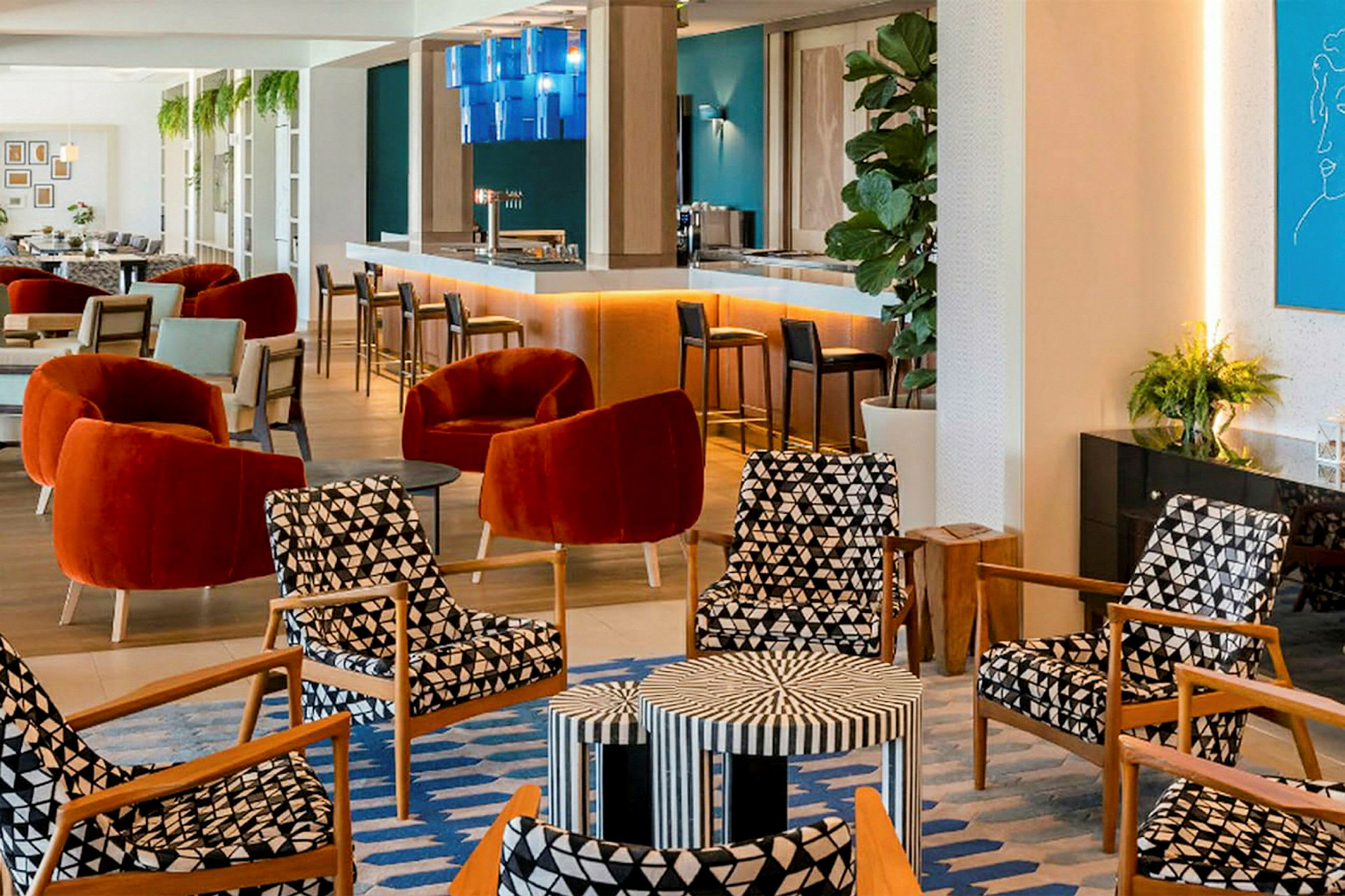 En modern lounge med bekväma stolar i röda och mönstrade färger, ett barsområde och väggdekorationer. (AI-genererad text)