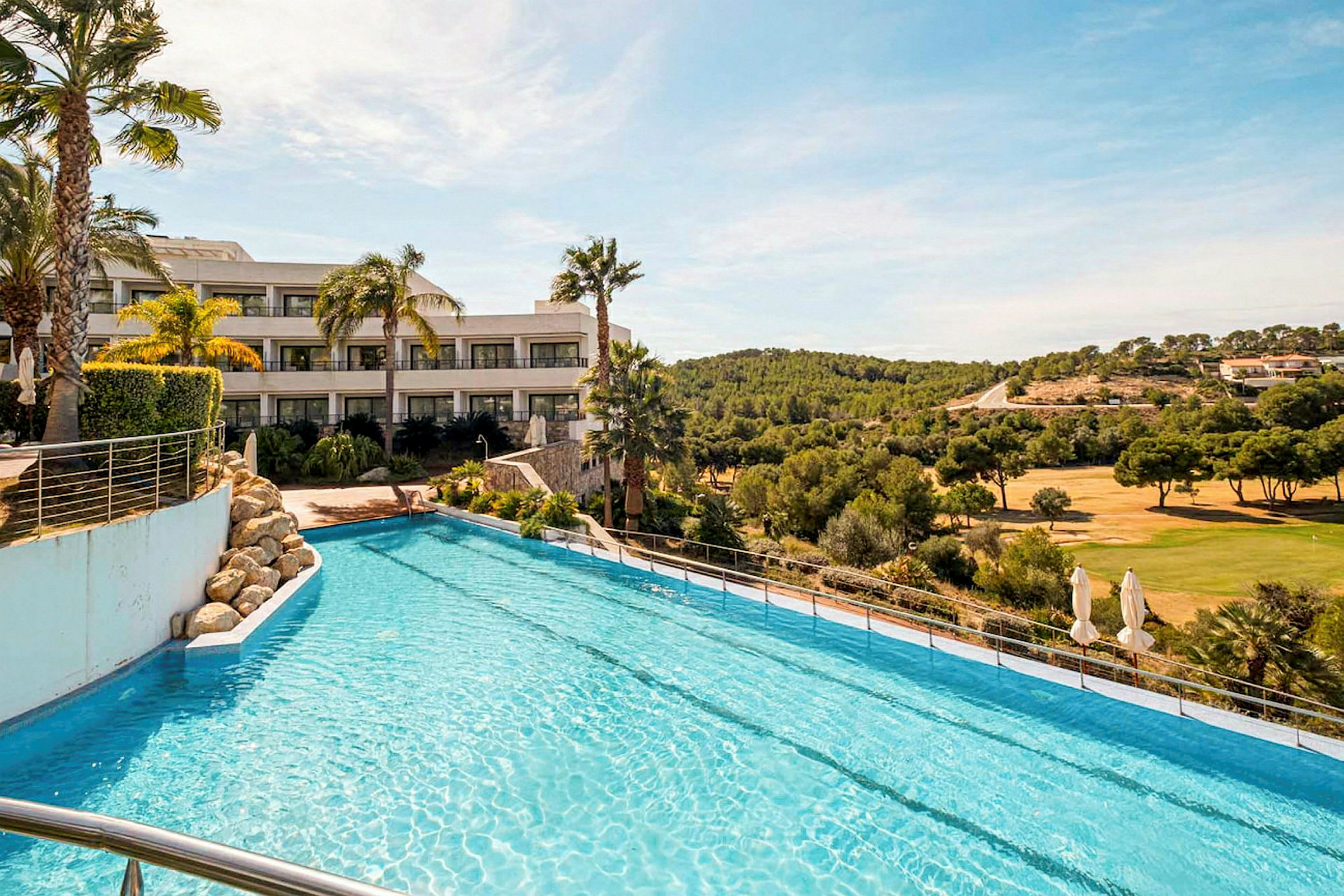 Ett hotell vid en pool, med utsikt över ett golfområde och skog i bakgrunden. (AI-genererad text)