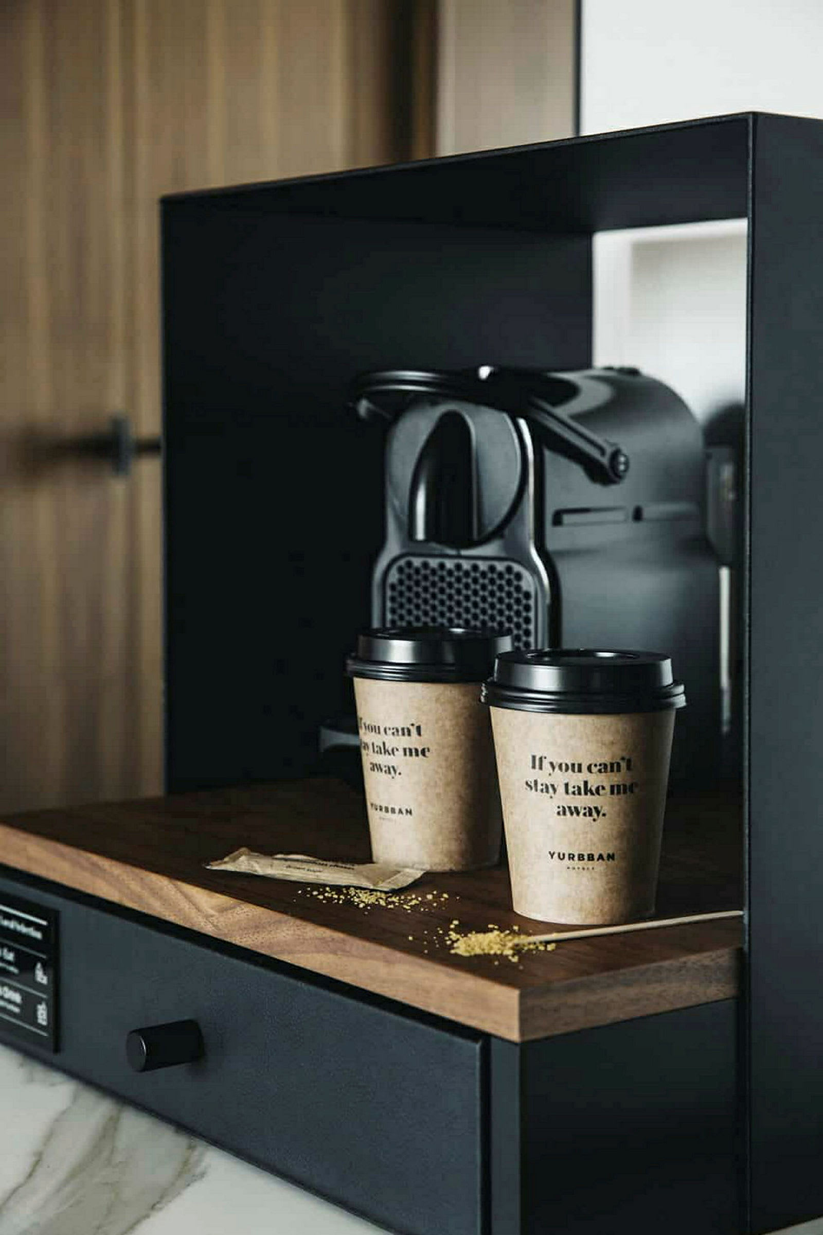 En kaffemaskin står på en mörk träbänk bredvid två kaffemuggar i papp. (AI-genererad text)