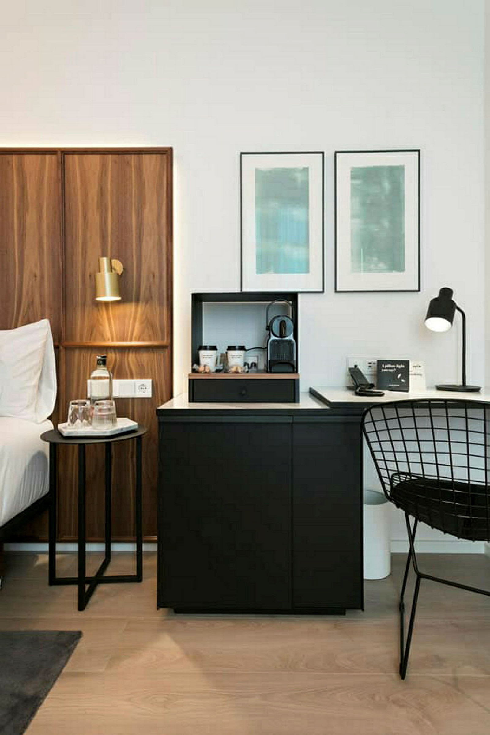 Ett hotellrum med en säng till vänster, ett litet bord med en flaska vatten och glas. På höger sida finns ett svart skrivbord med en kaffemaskin och en stol. (AI-genererad text)