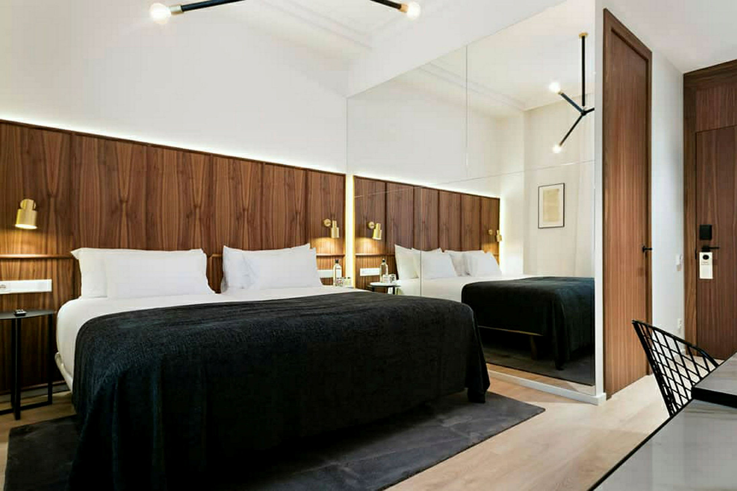 Ett modernt hotellrum med en stor säng, träpaneler på väggen och speglar som ger rummet en rymd. (AI-genererad text)